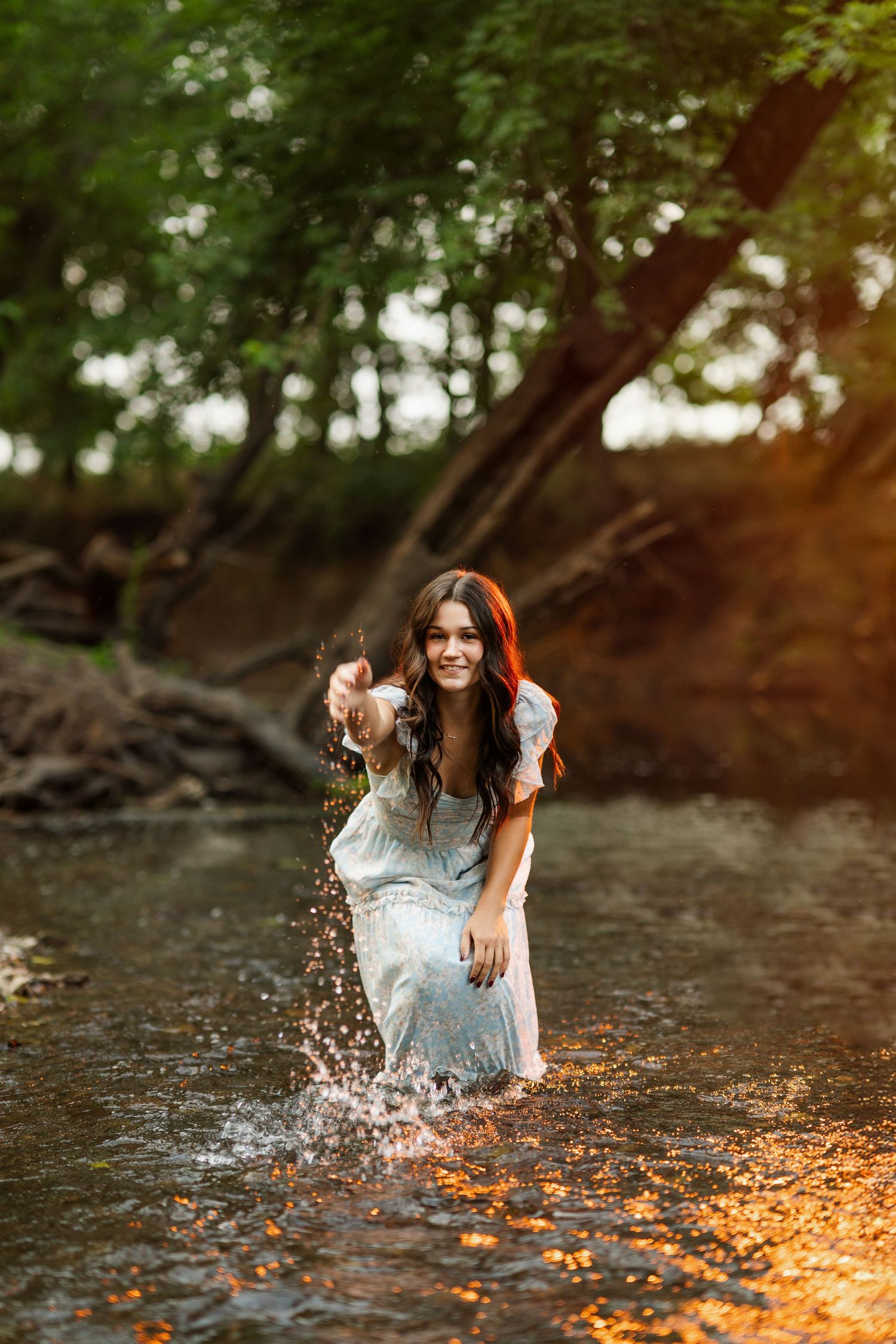 Water splashes dramatically around a light dress during a sunset creek photoshoot.