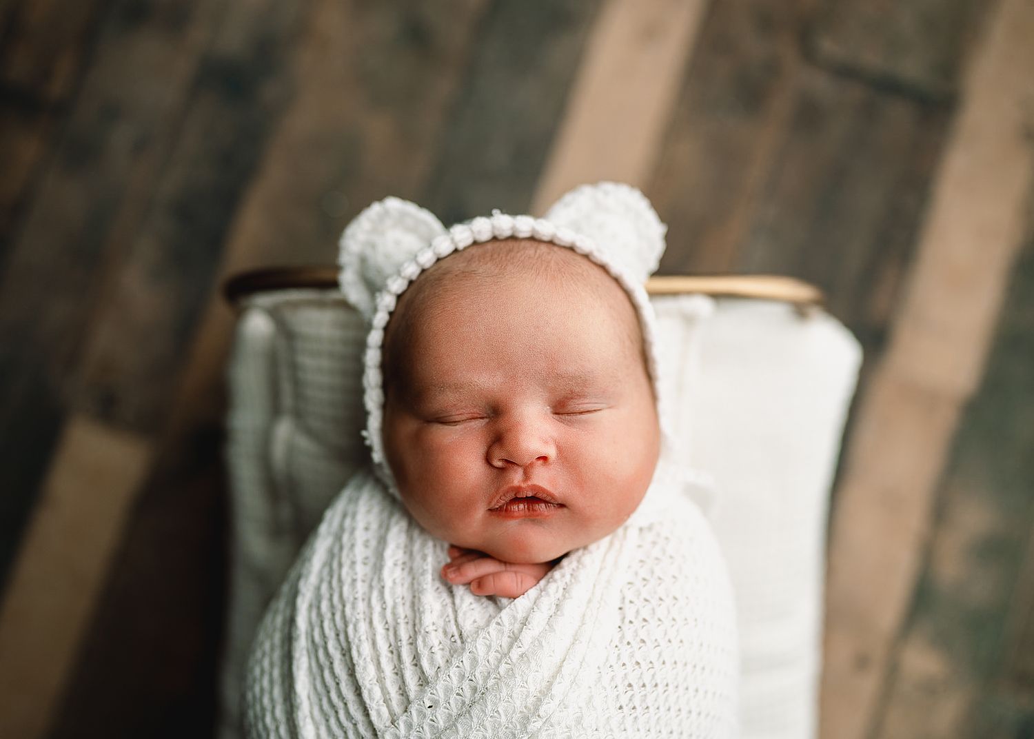 Newborn baby wrapped in white knit blanket with matching hat sleeping peacefully.