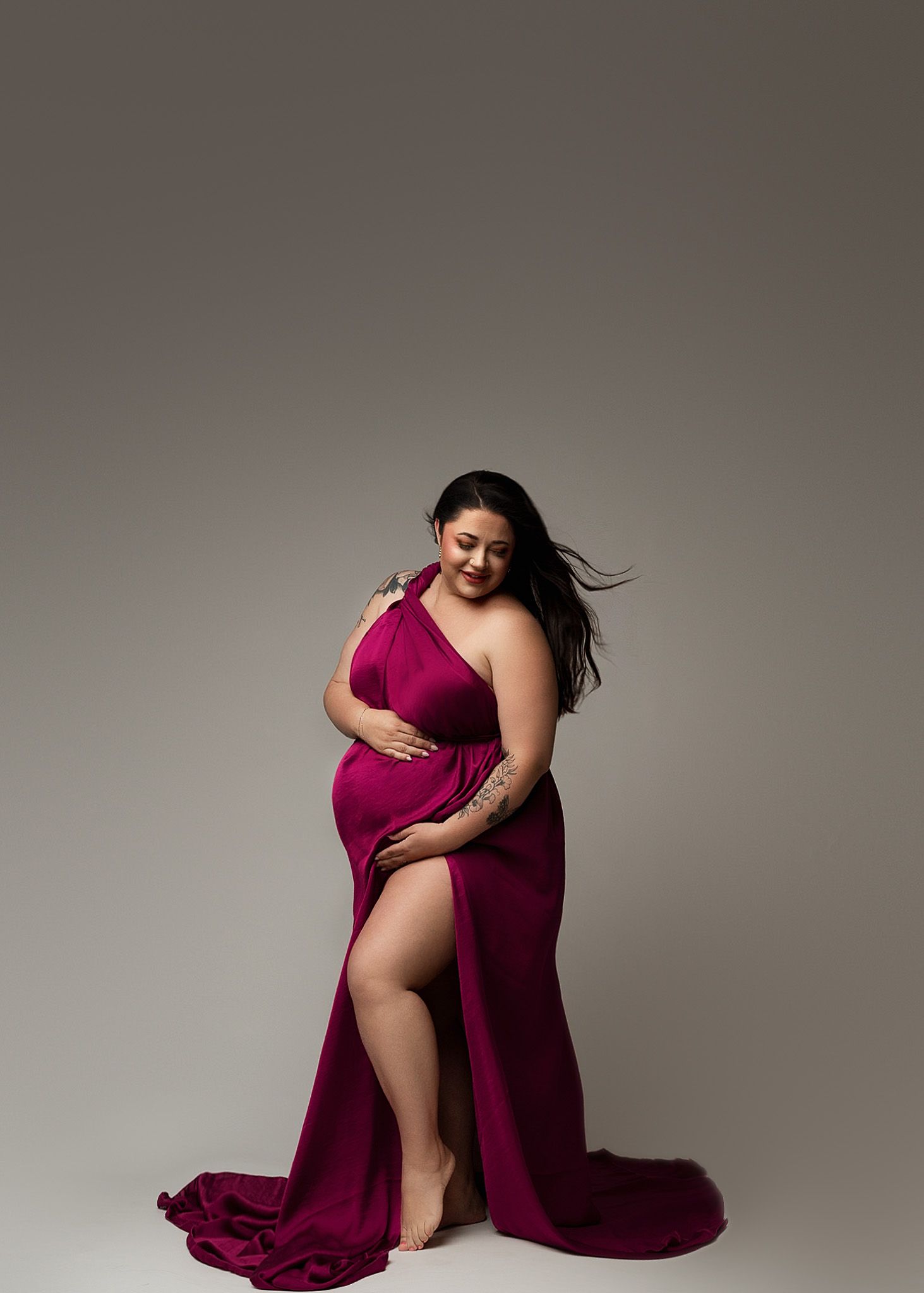 Dramatic burgundy one-shoulder gown with flowing train captured in studio lighting.
