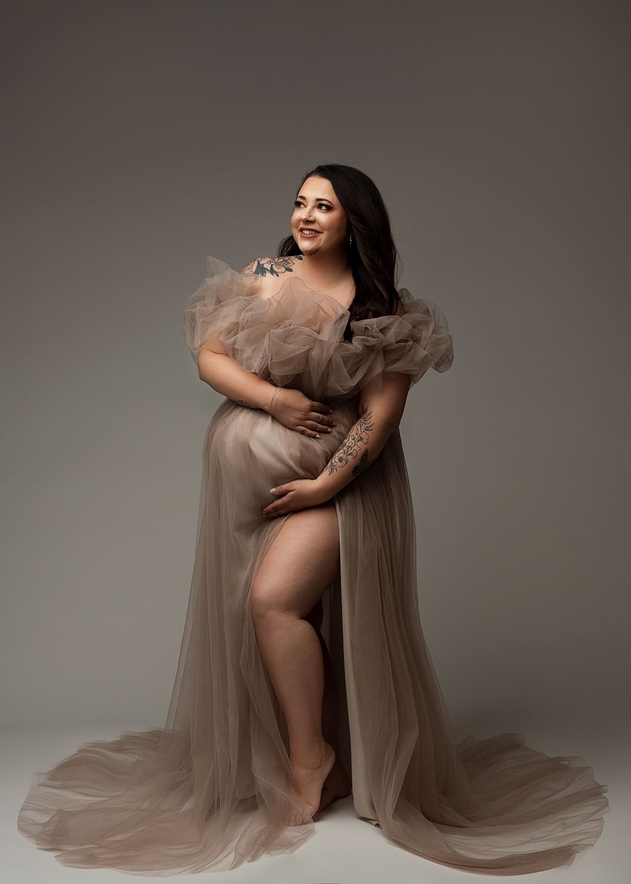 Artistic maternity photos in flowing beige tulle dress against dark background.