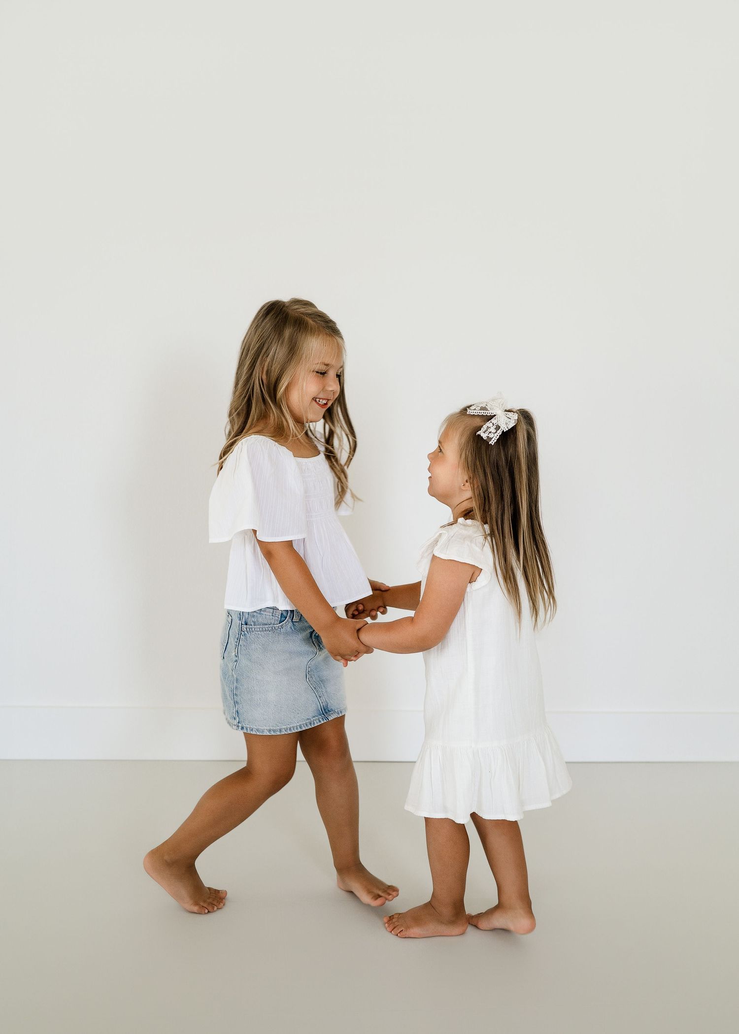 Two children in white outfits playing together against a white wall.