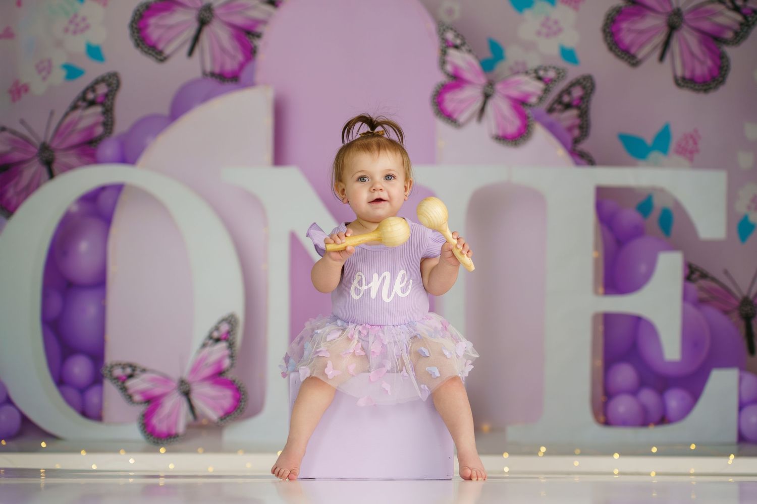 Decorated photo setup with purple butterflies and balloons for cake smash session.