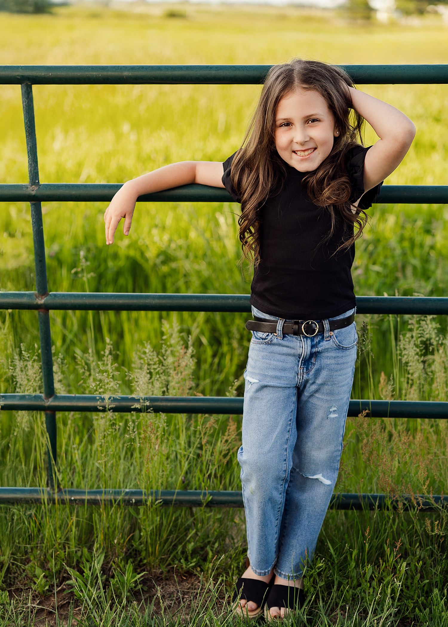 Casual outdoor portrait session near green field with metal fence.