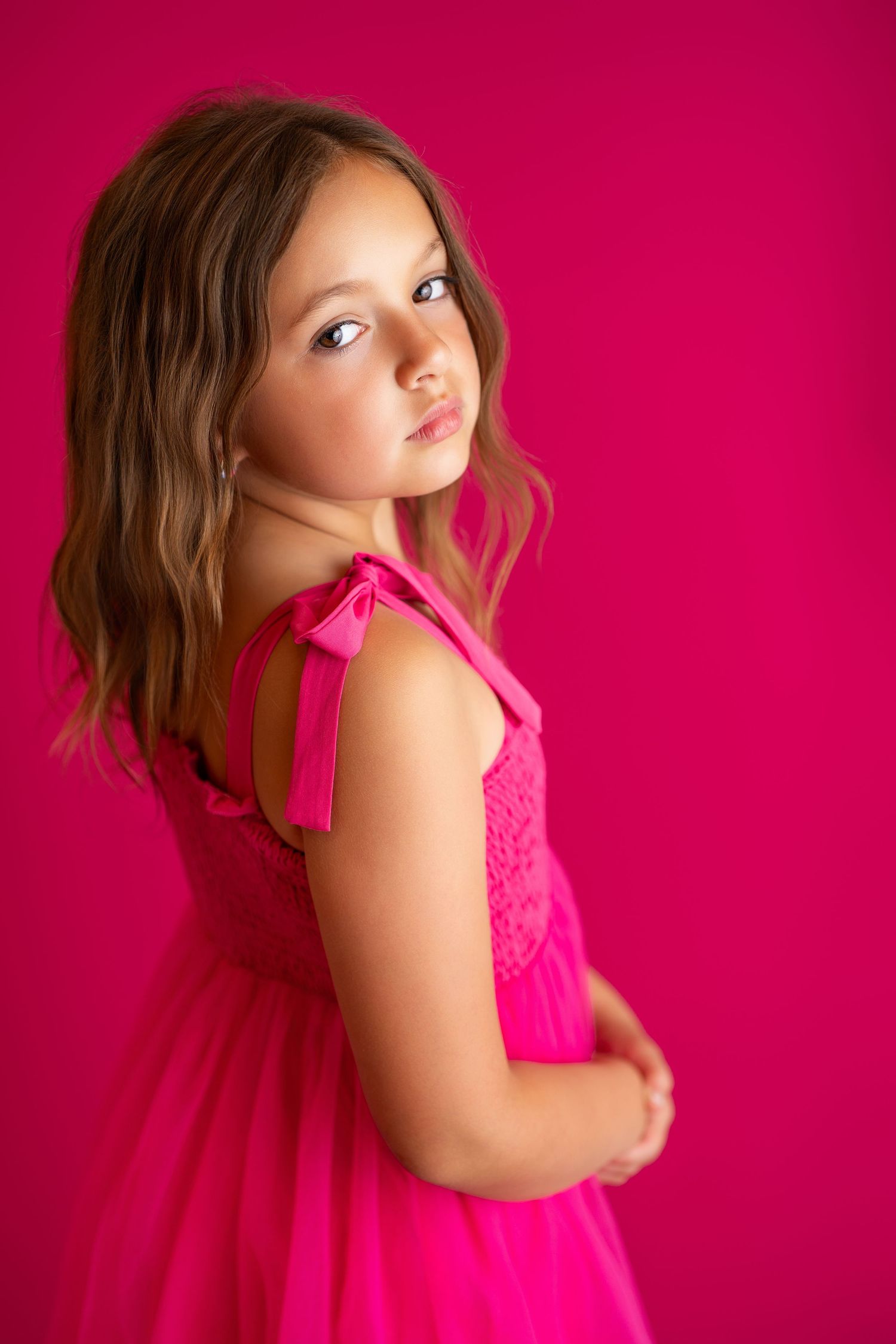 Artistic portrait poses in bright pink tulle dress against magenta backdrop.