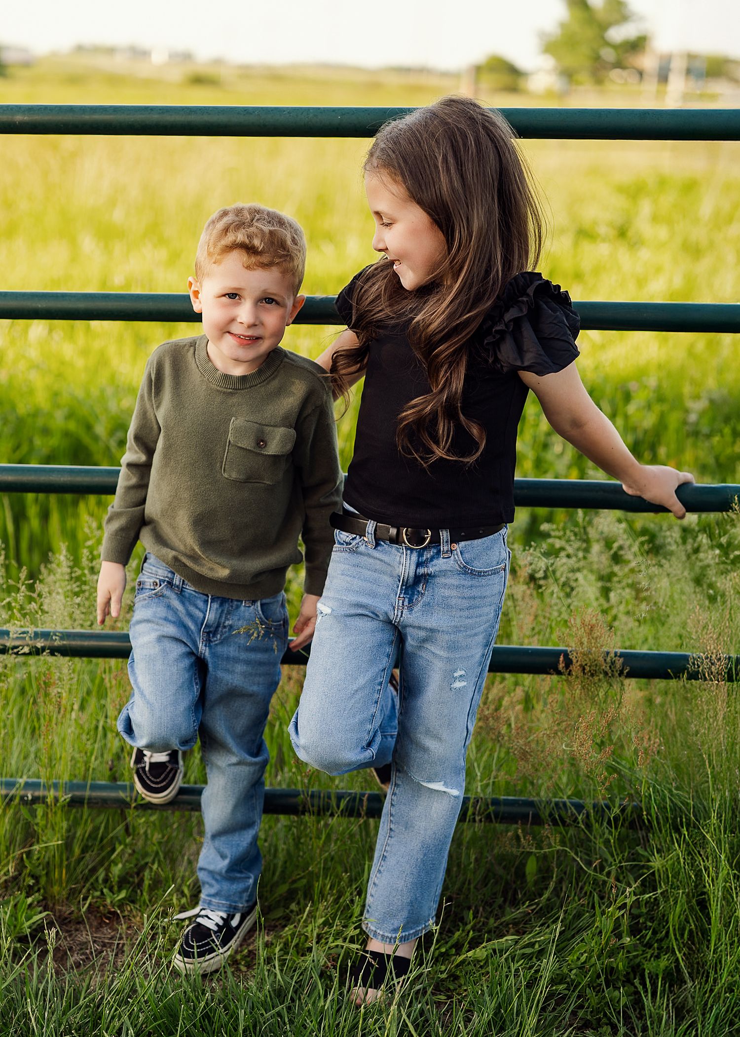 Two people sitting on green bench in field with tall grass at sunset.
