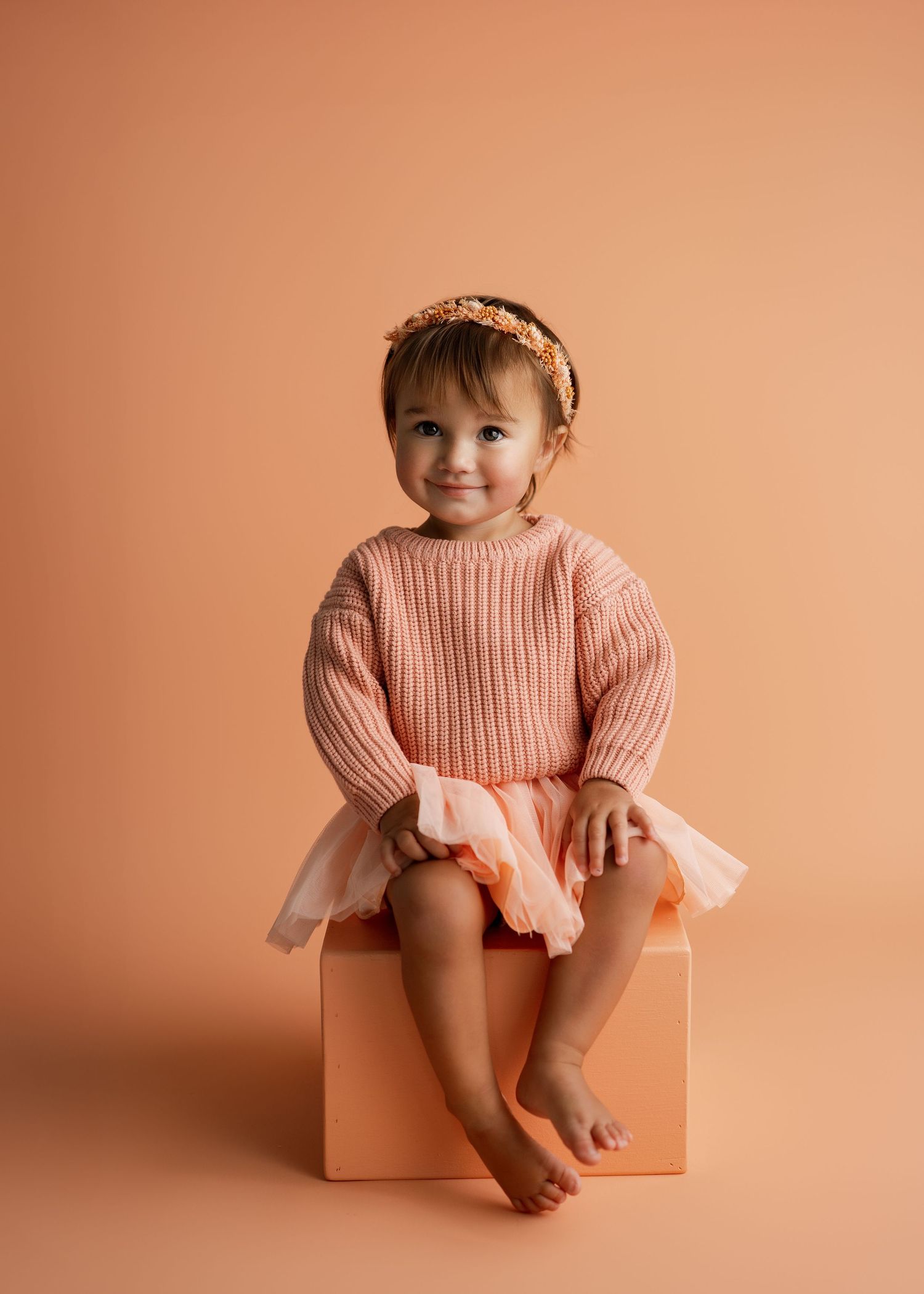 Studio portrait series with peach-colored knitwear against warm backdrop.