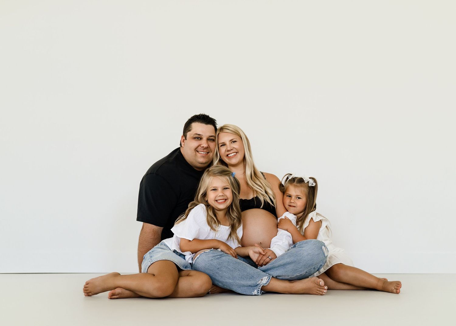 Family lying together on white background in casual clothing for lifestyle portrait session.