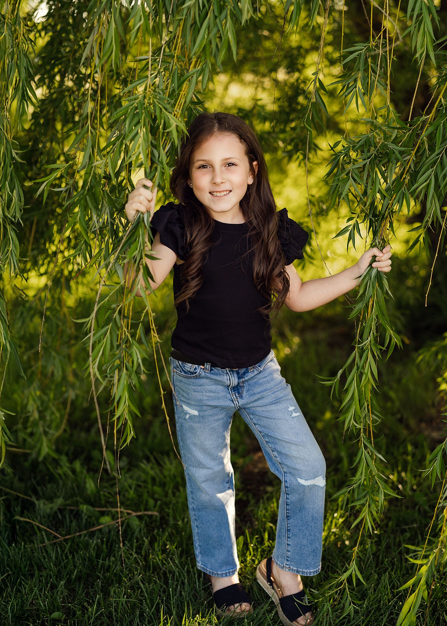 Child holding willow tree branches while playing outdoors in casual clothing.