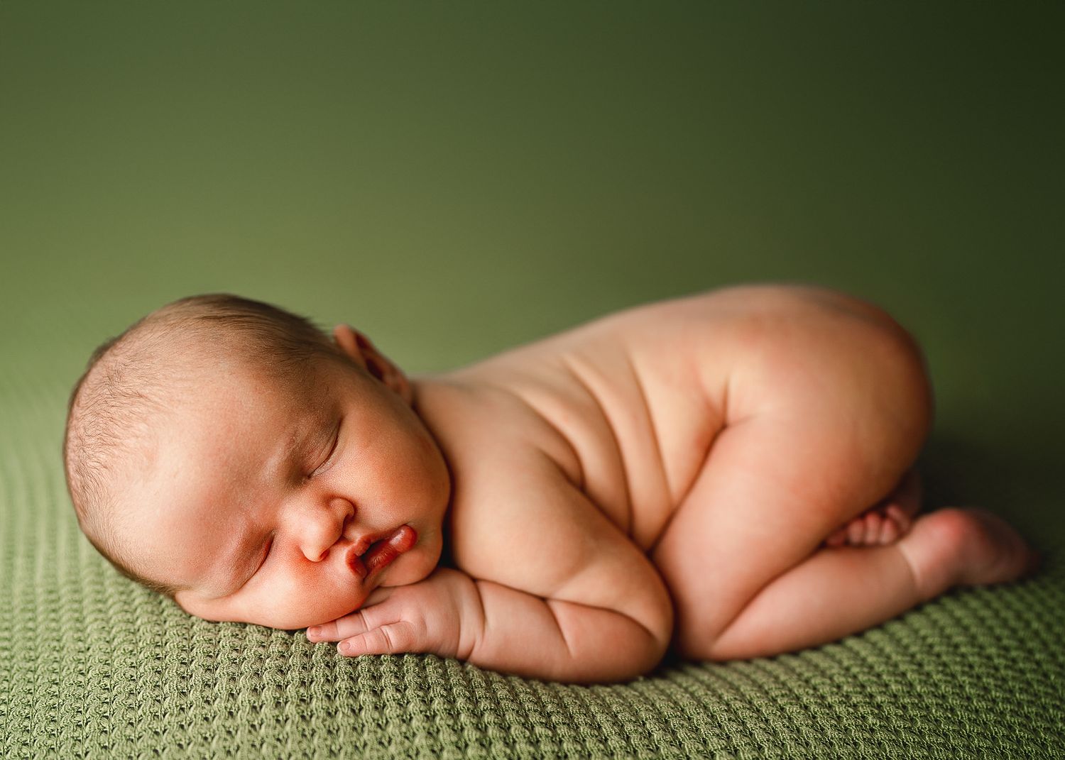 Artistic newborn photography with baby sleeping on green textured backdrop.