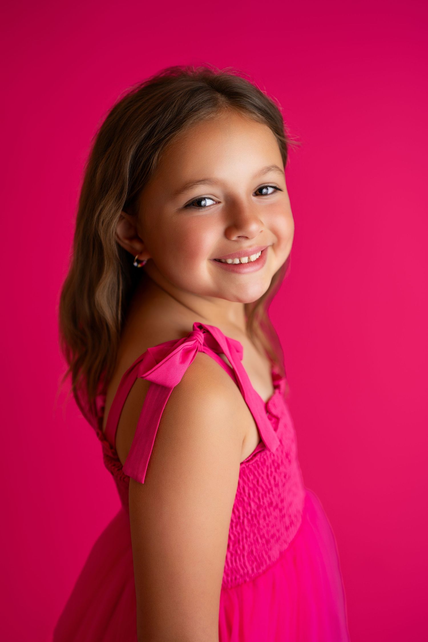 Portrait of young girl in bright pink dress against vibrant pink background.