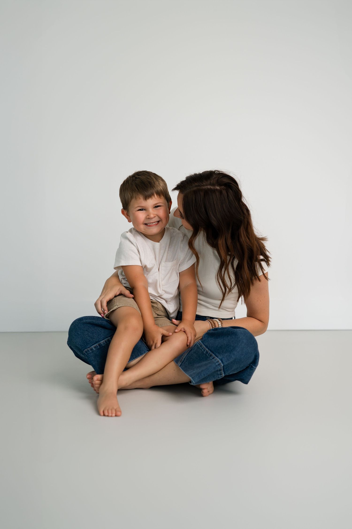 Two people in casual attire share a tender moment against white backdrop.