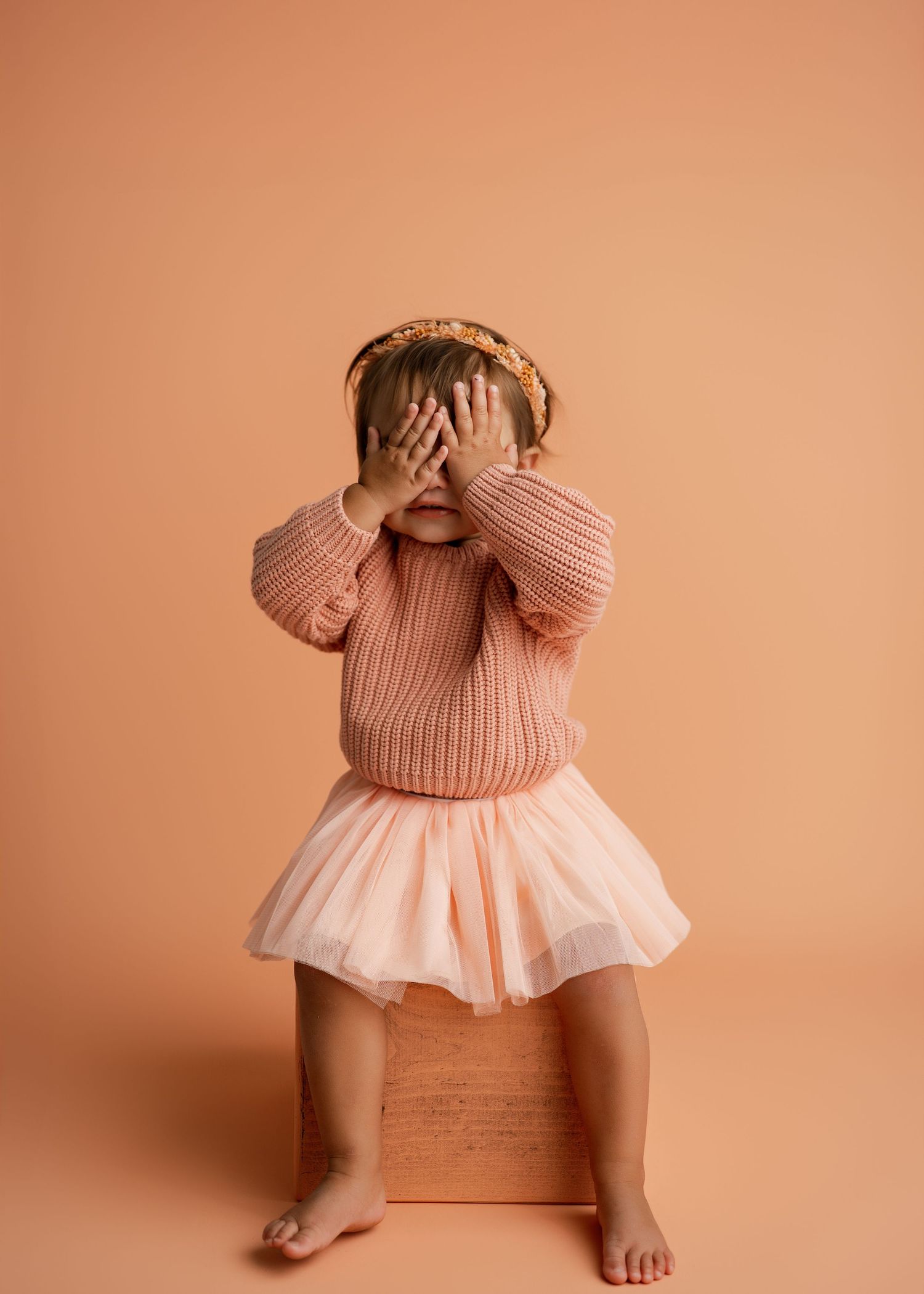 Playful poses in a peach-colored knit sweater dress against warm neutral backdrop.