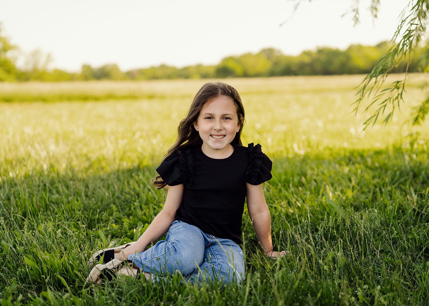Outdoor portrait session in grassy field during golden hour with black fence.