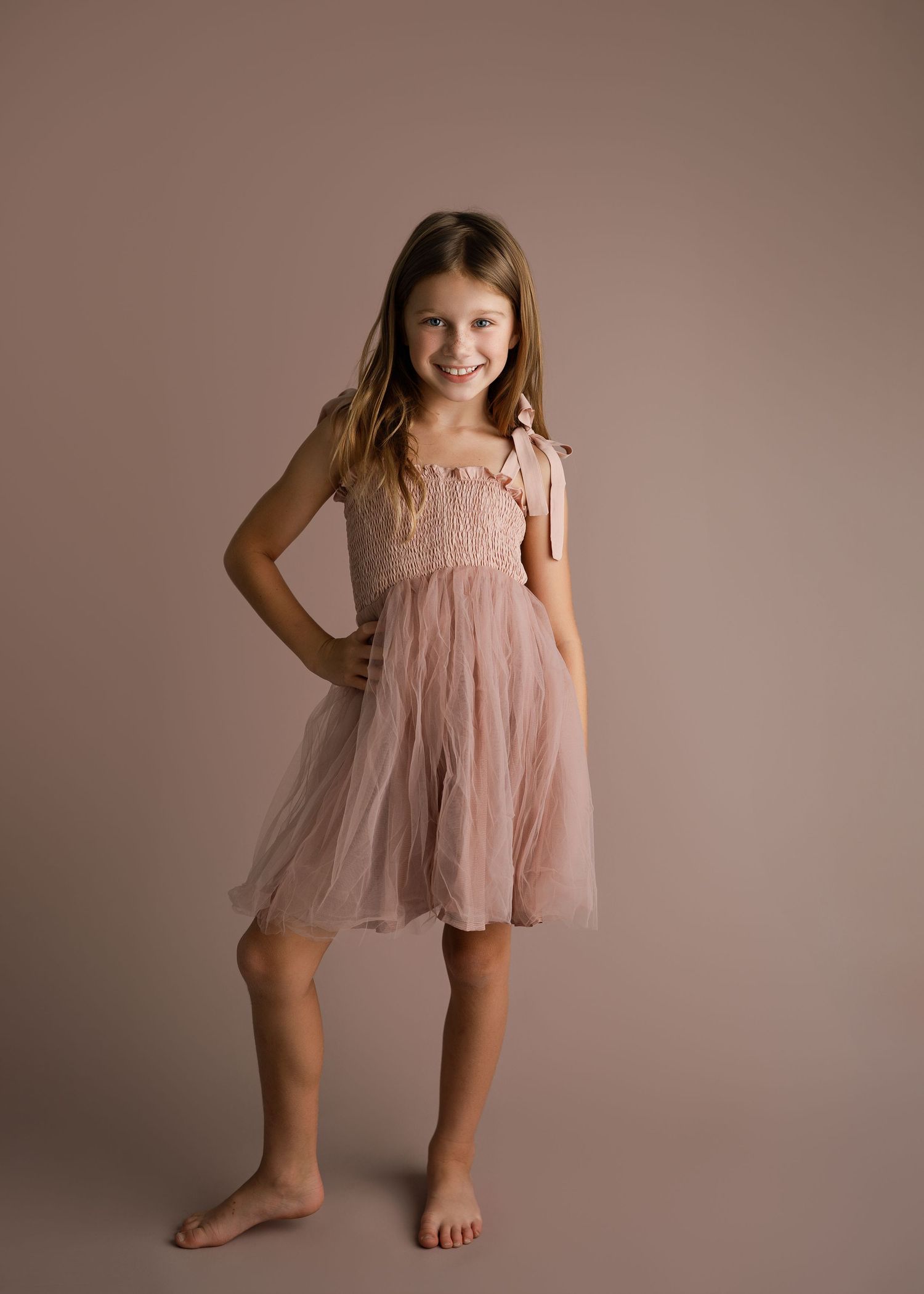 Child in pink tulle dress strikes playful dance poses in studio setting.