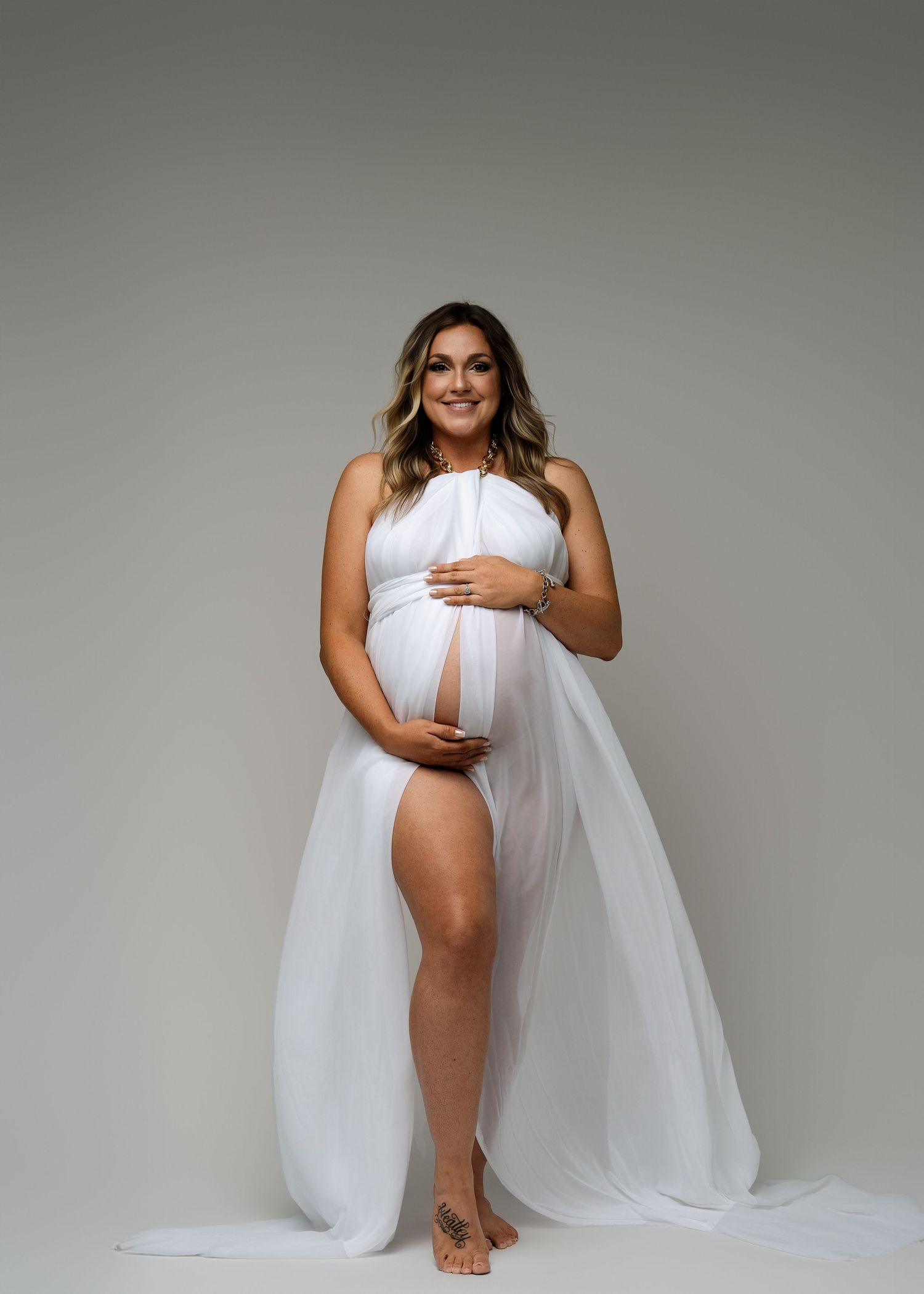 Modern maternity photoshoot featuring white draped fabric against light gray background.