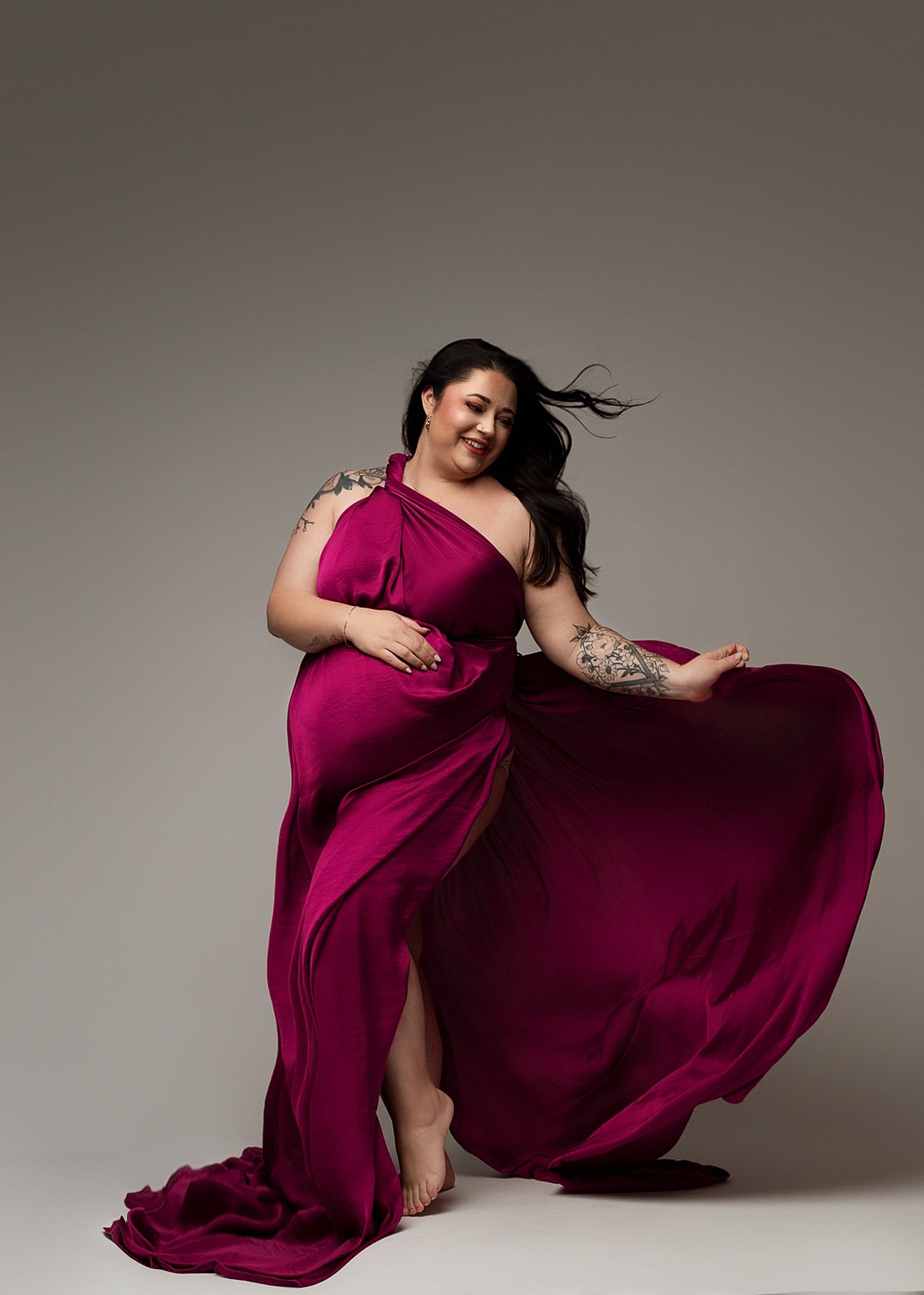 Artistic maternity photoshoot featuring a flowing burgundy dress against a neutral backdrop.