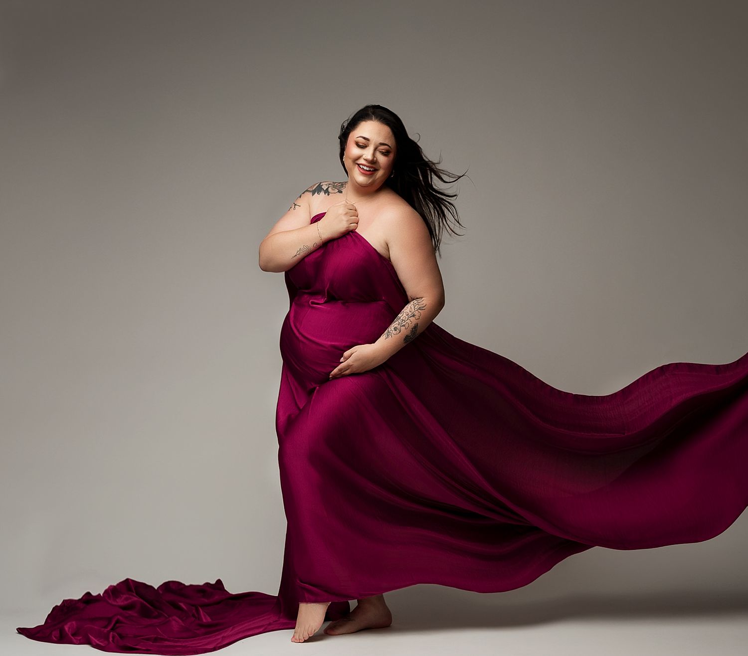 Flowing burgundy gown with dramatic movement captured against grey backdrop in elegant fashion photo.