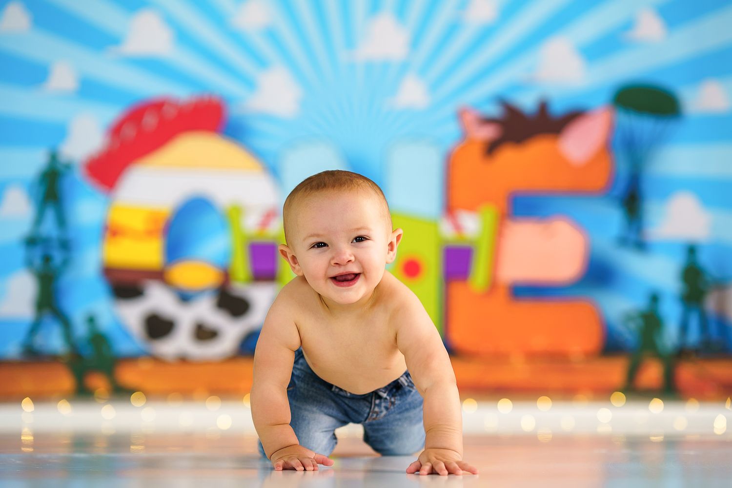 Smiling baby in blue outfit crawling against colorful pirate-themed backdrop.