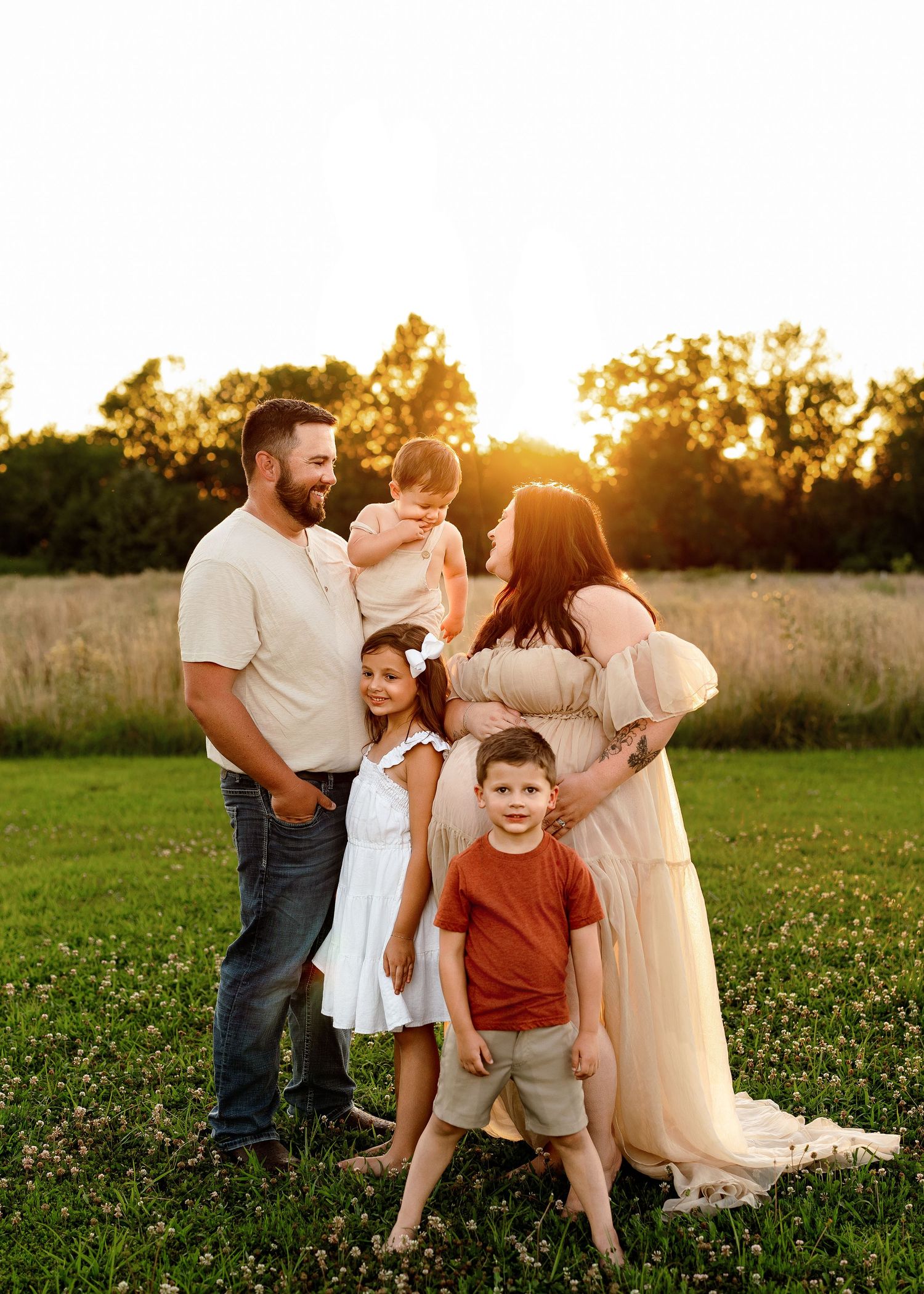 Family photo session in a sunlit field with coordinated neutral outfits.