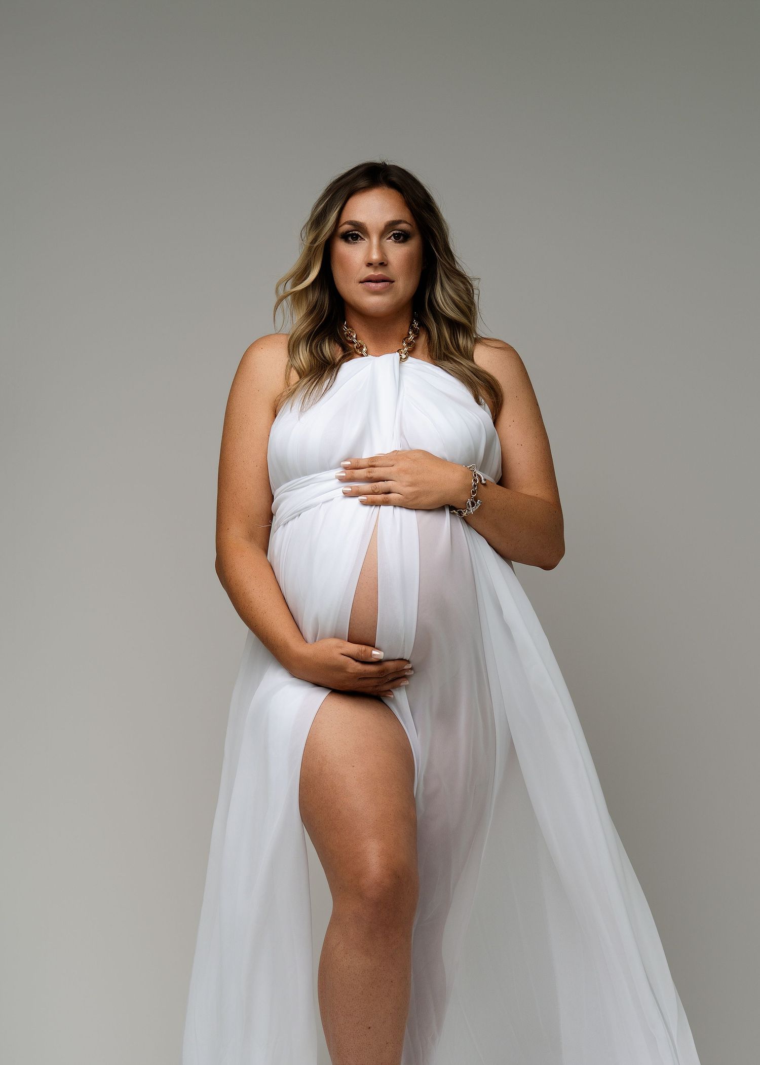 Artistic maternity photoshoot with flowing white fabric against a neutral gray backdrop.