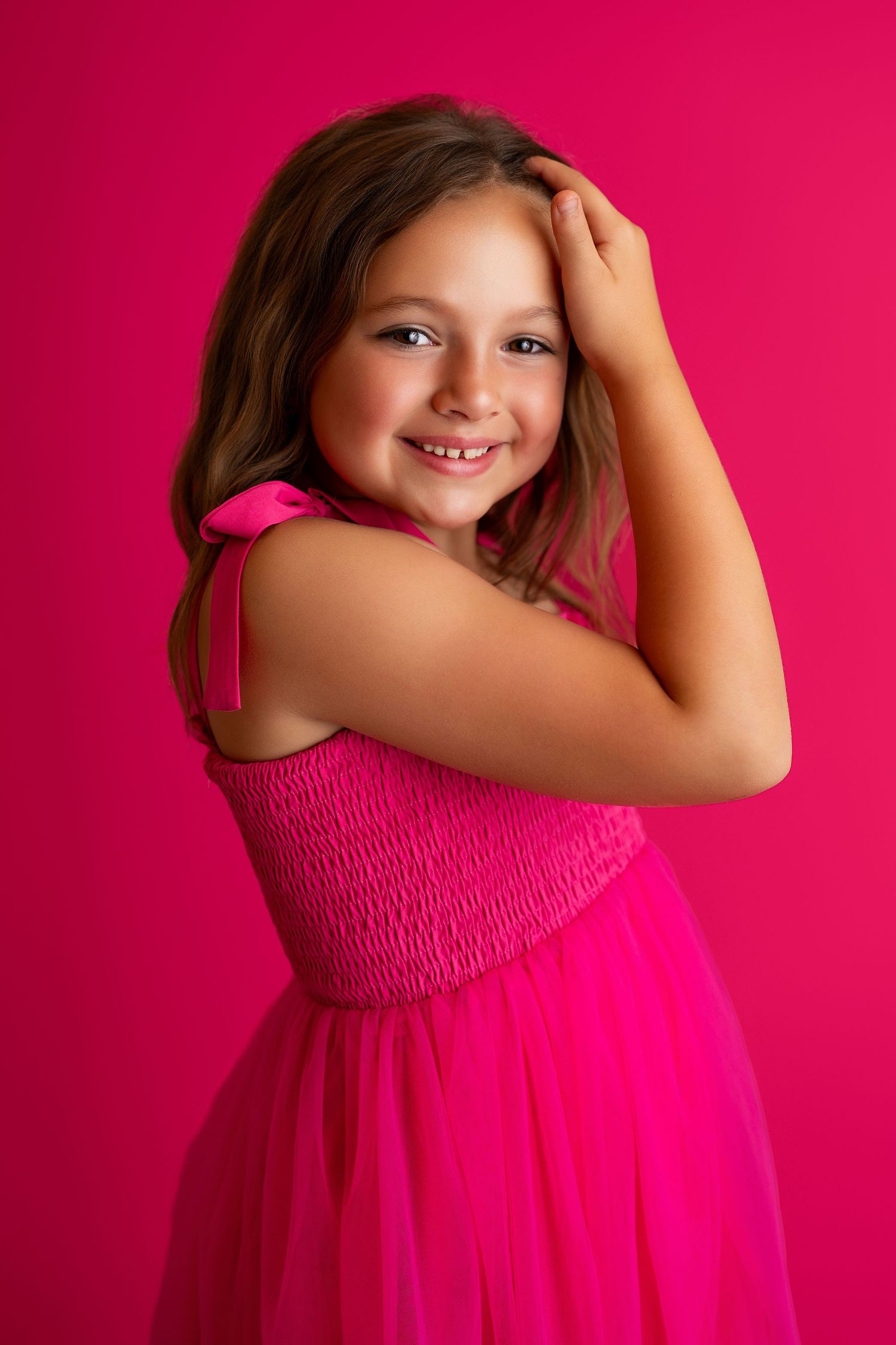 Child in hot pink dress twirls and smiles against magenta background.
