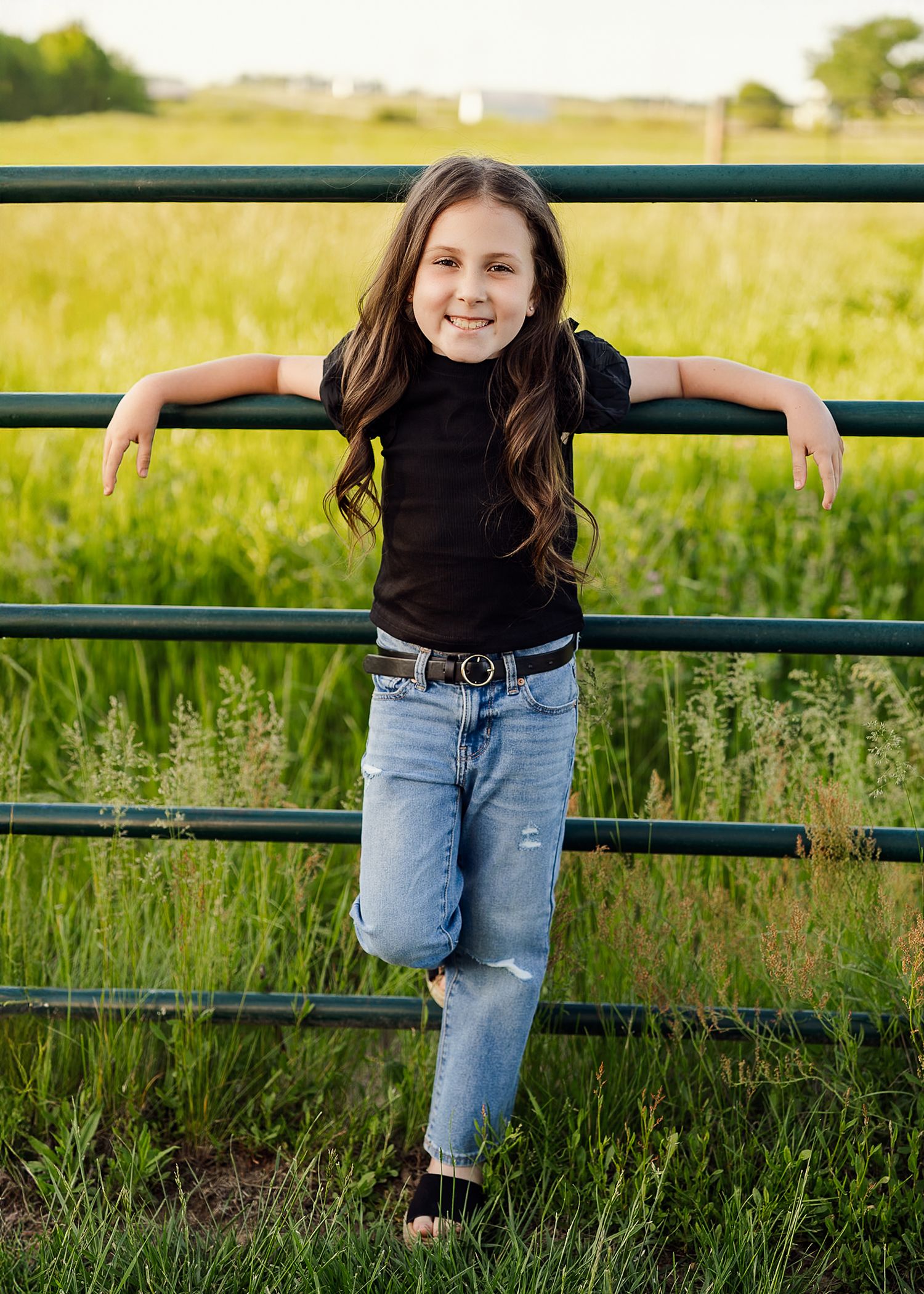 Playful outdoor photoshoot with metal fence and tall grass in background.