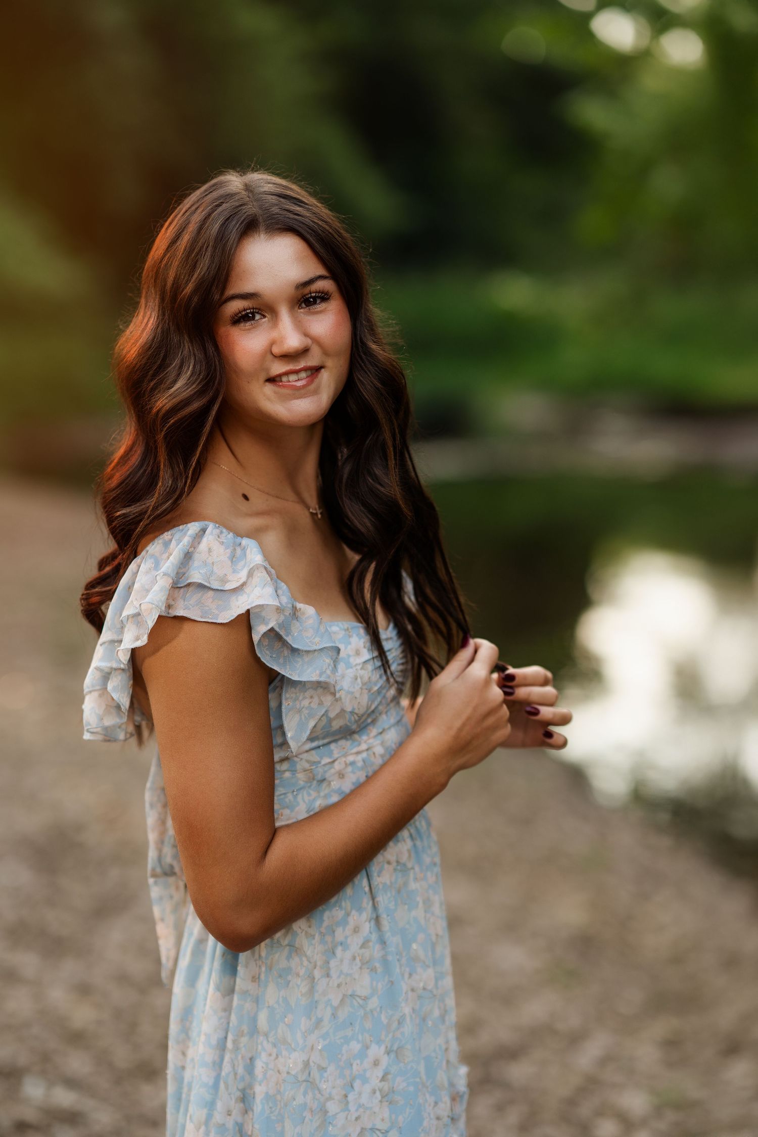 Portrait session by a pond featuring a light blue floral dress with ruffled sleeves.