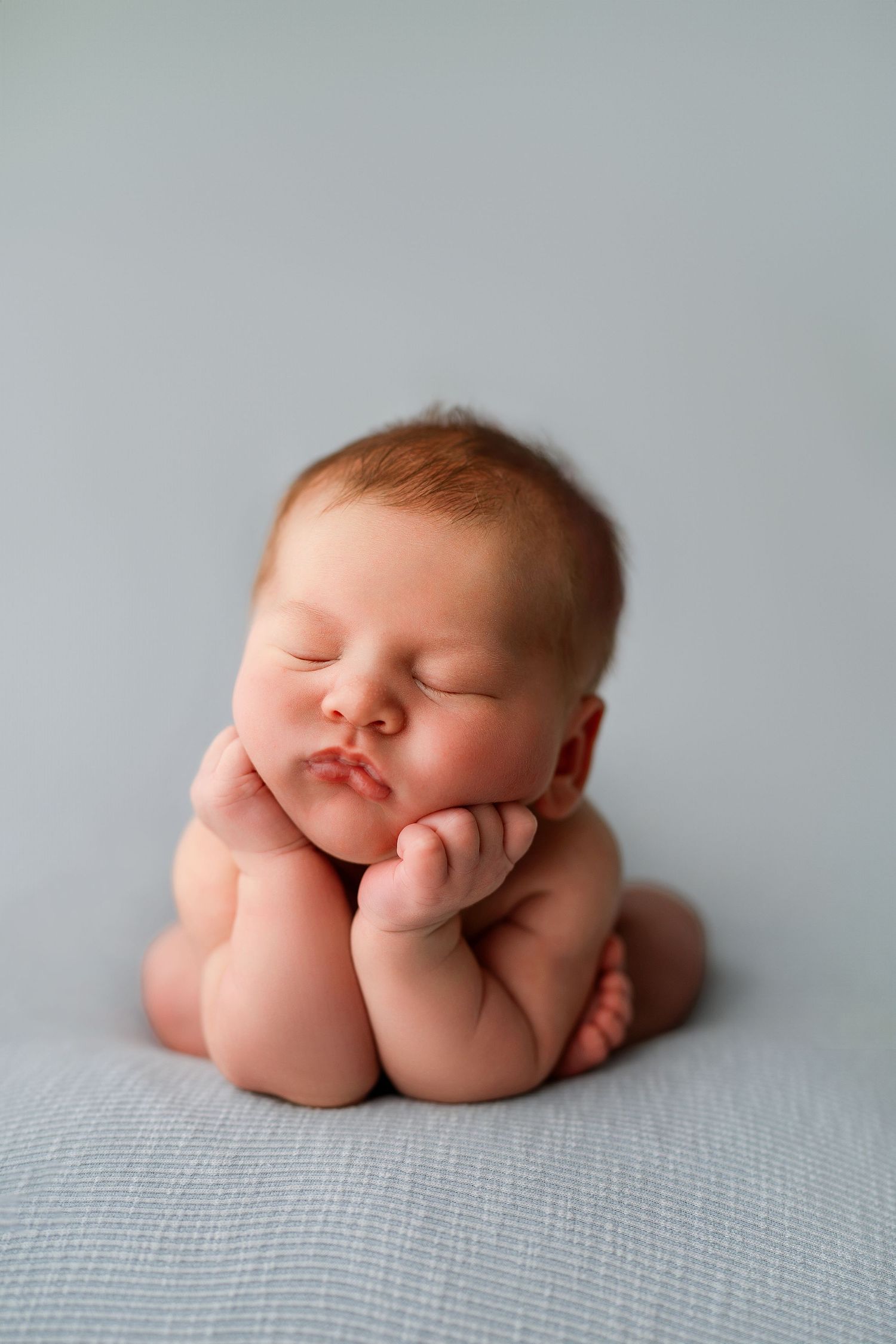 Sleeping newborn baby posed curled up on textured gray blanket.