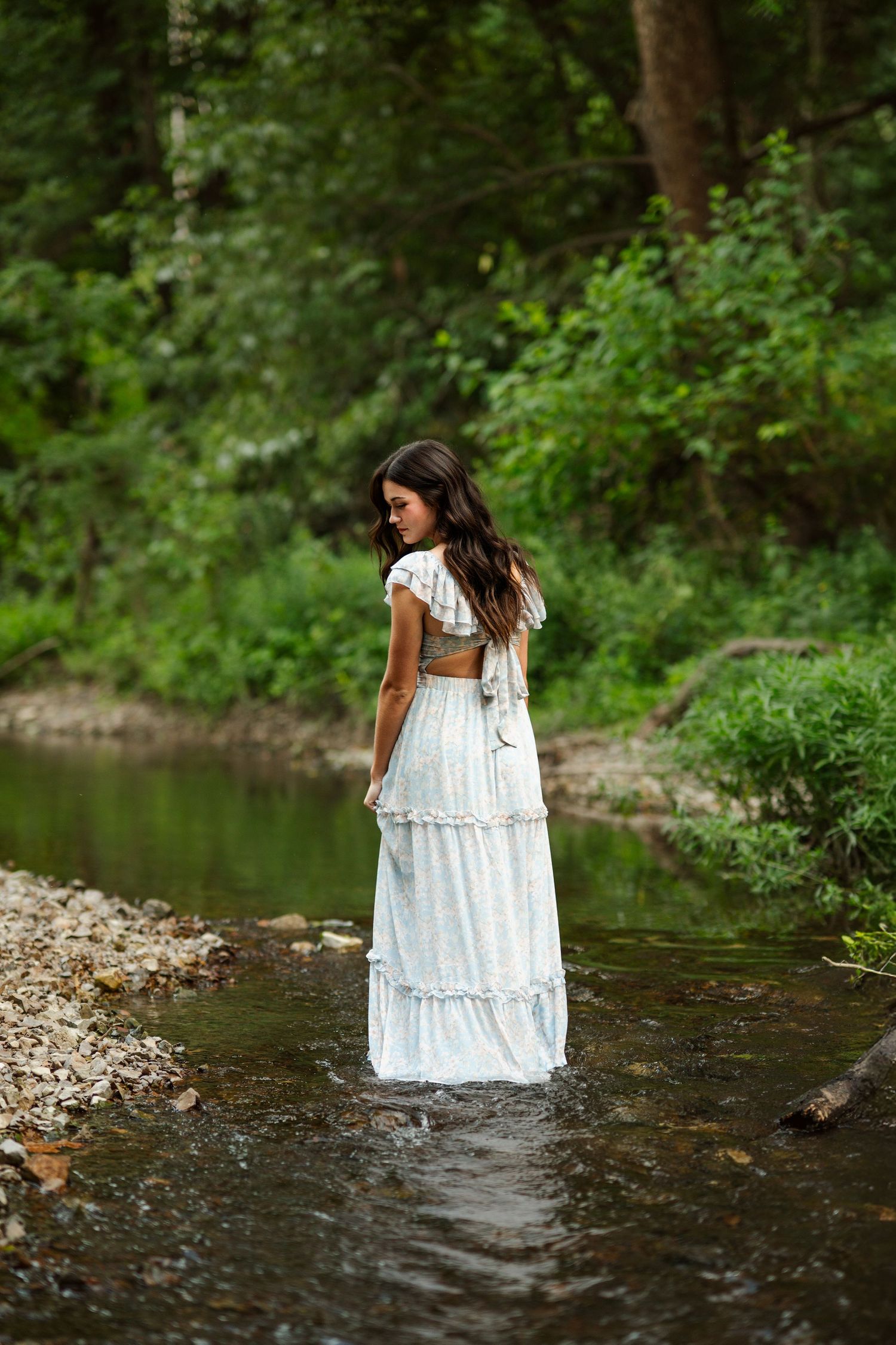 A romantic portrait session shows a white dress flowing in shallow stream water.