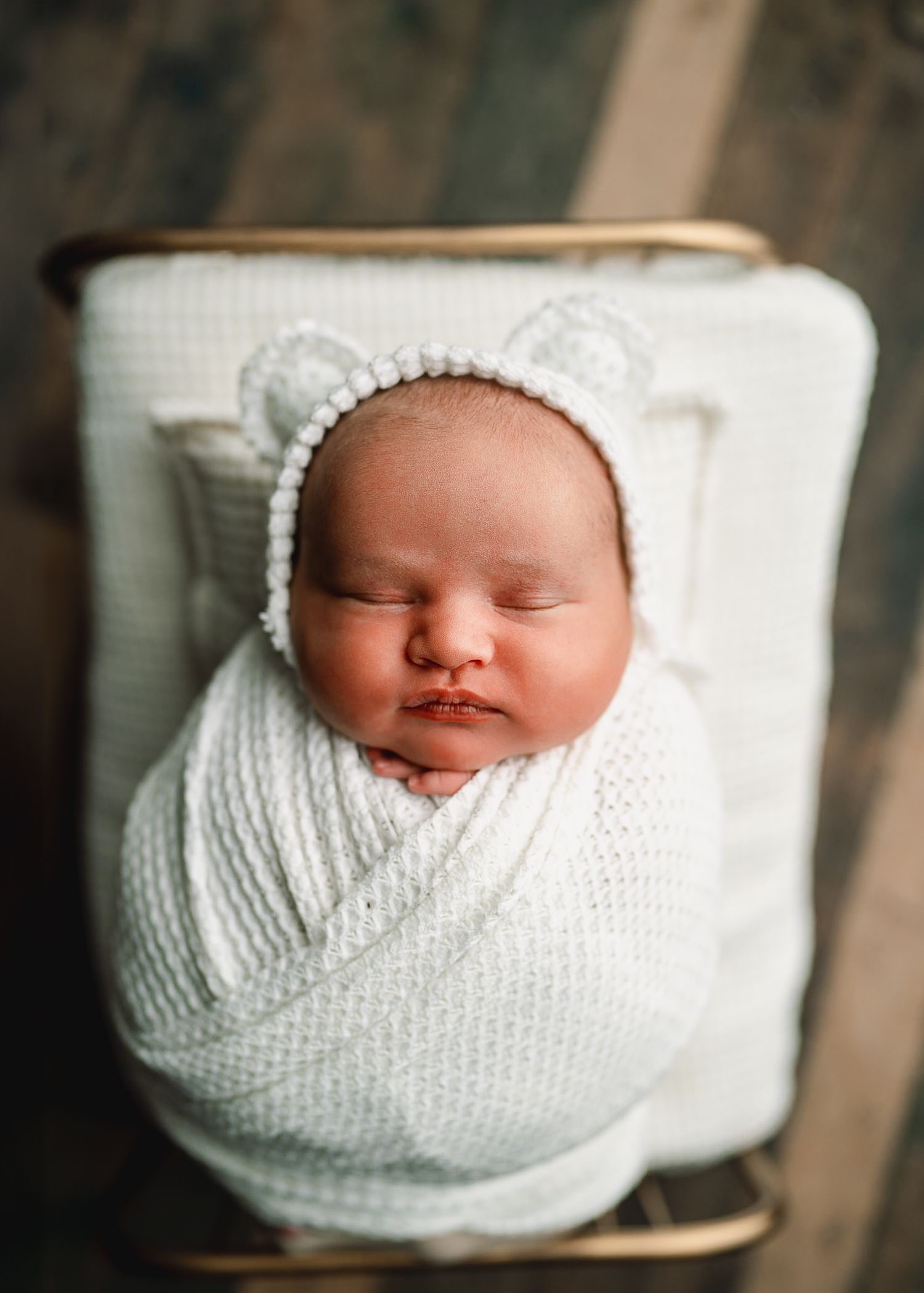 Sleeping newborn wrapped in white knit blanket in wooden container.