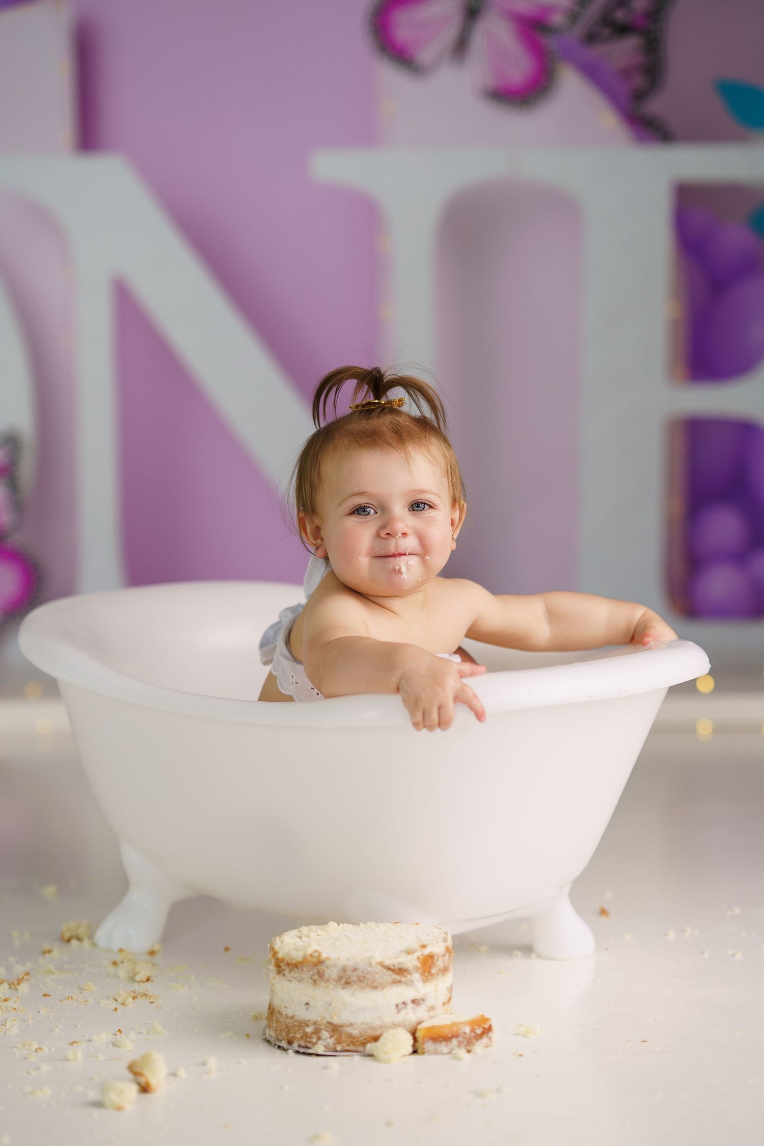 Baby posing in decorative white bathtub with cake crumbs during photo session.