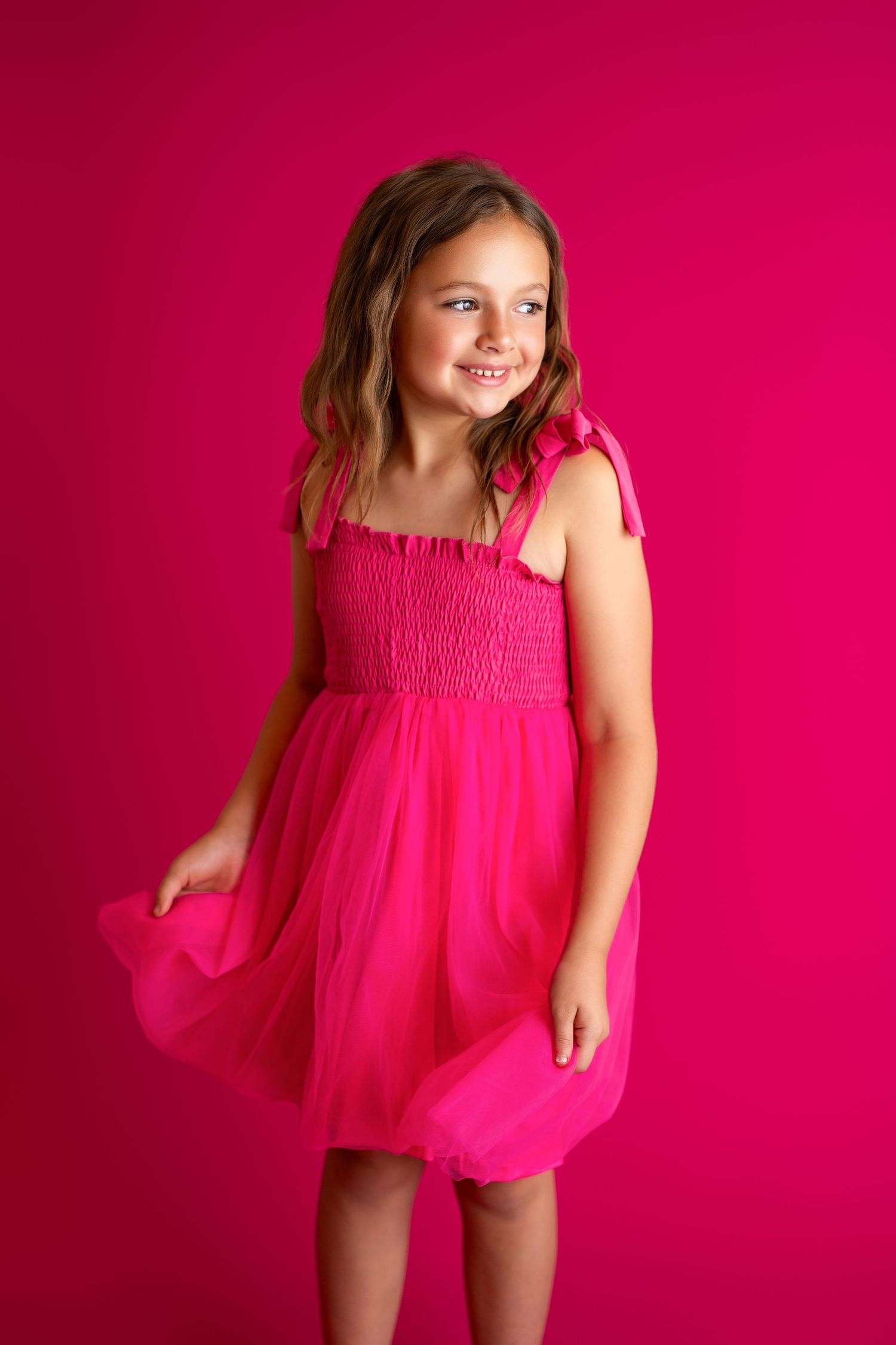 Playful pose in bright pink tulle dress against magenta studio background.