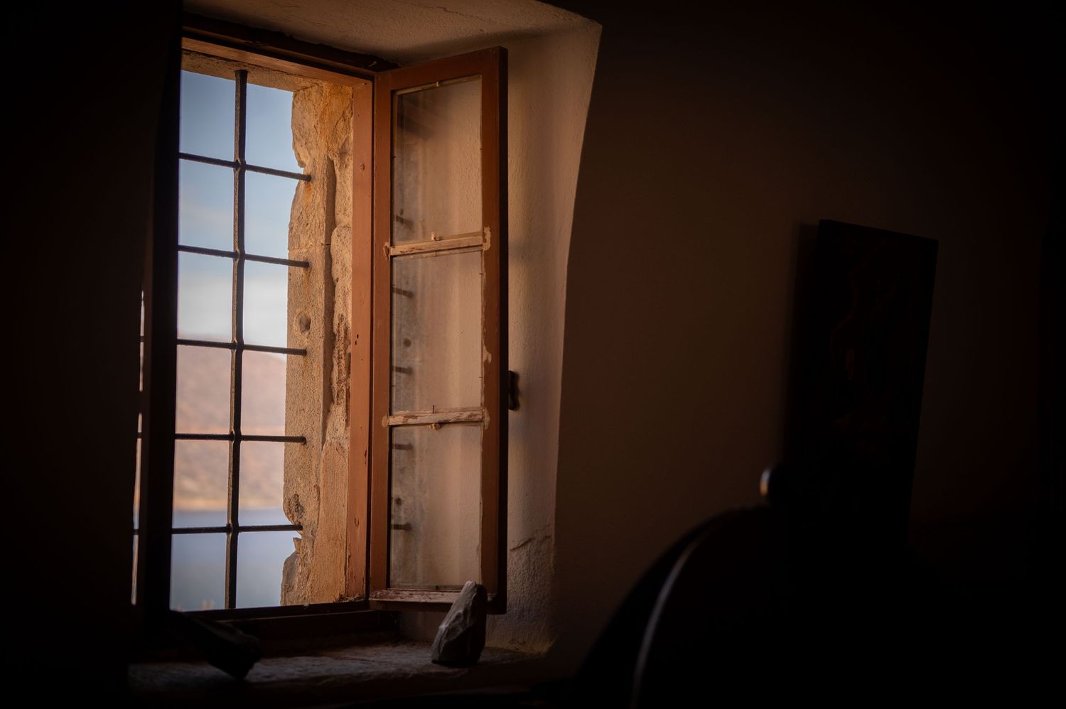Dark interior room with sunlight streaming through wooden shuttered windows creating dramatic shadows.