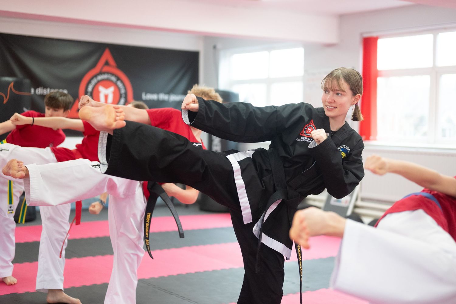 Martial arts training session with students practicing kicks on red mats.