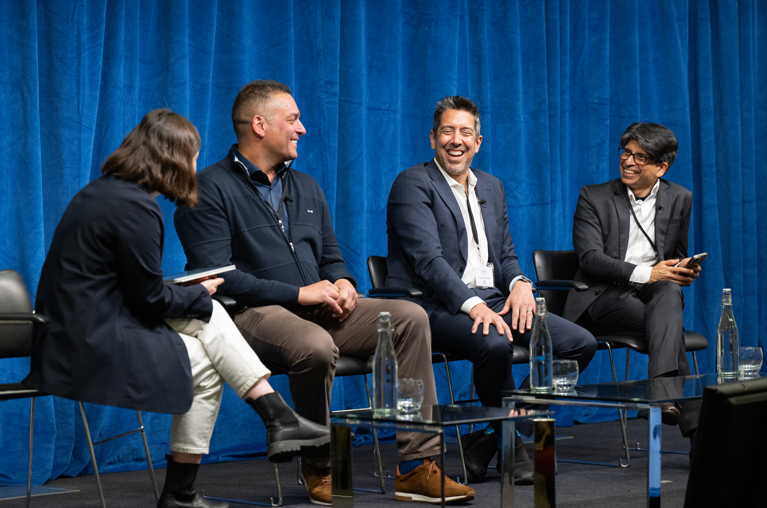 Panel discussion with business professionals seated on stage with blue backdrop.