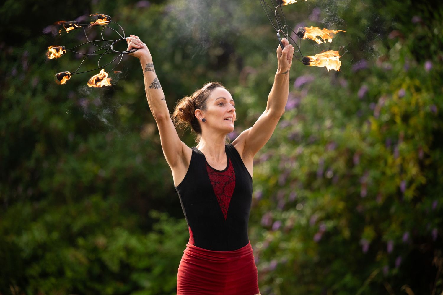 Fire dancer performing with flaming torches at dusk in outdoor setting.