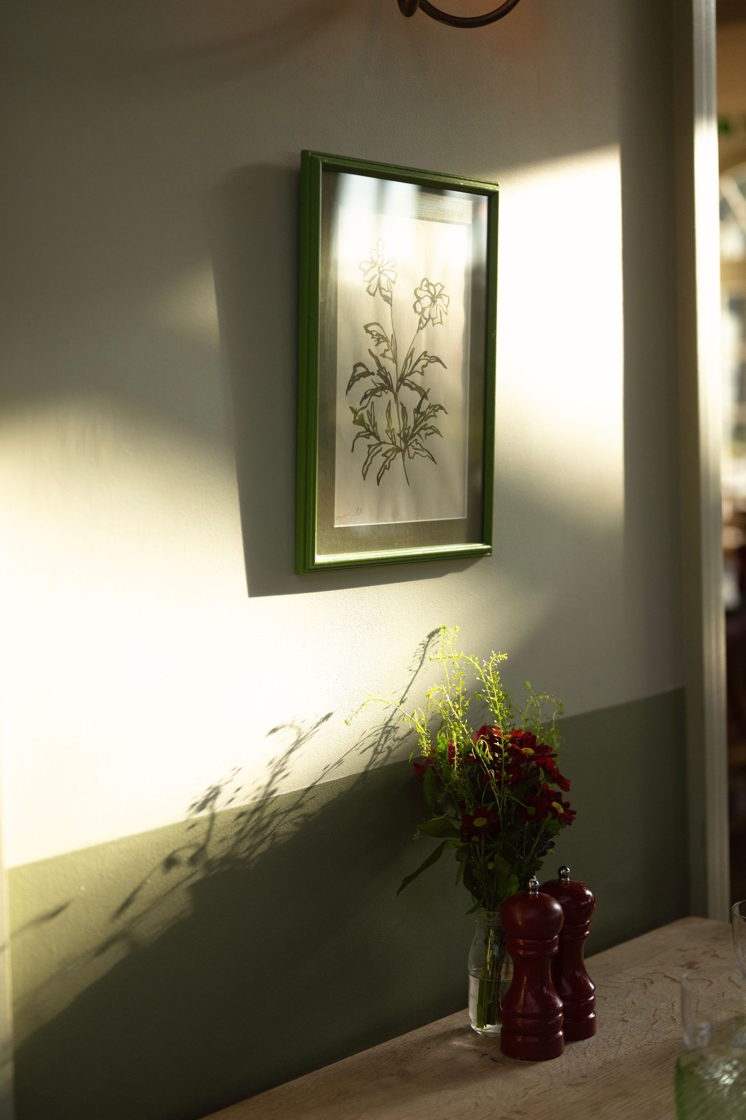 Minimalist hallway with framed botanical prints and shadows cast on sage green walls.