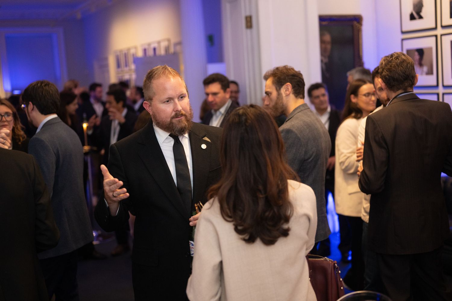 Formal evening networking event with blue lighting and attendees mingling in a gallery space.