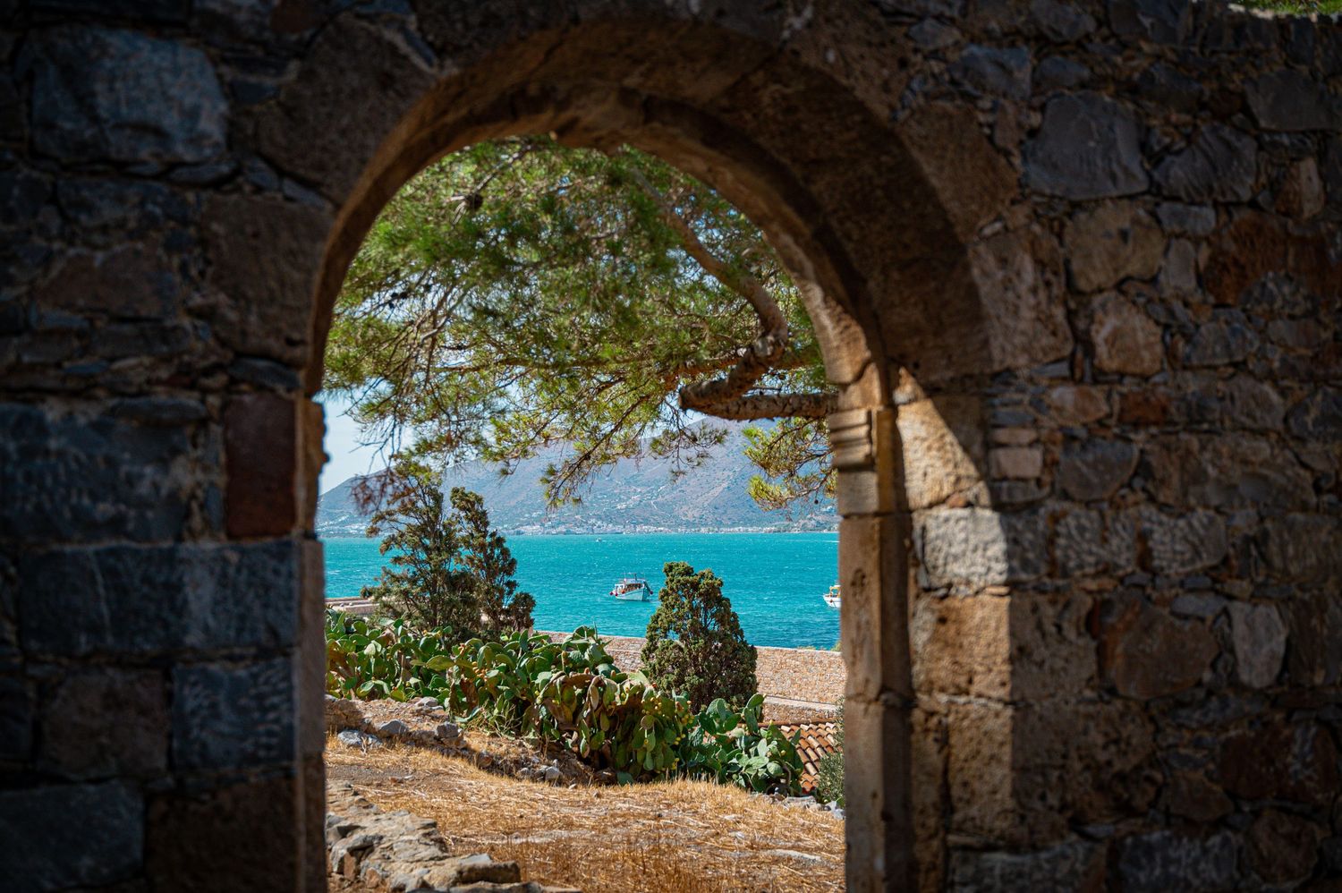 Stone archway framing a stunning turquoise ocean view with mountains in the distance.