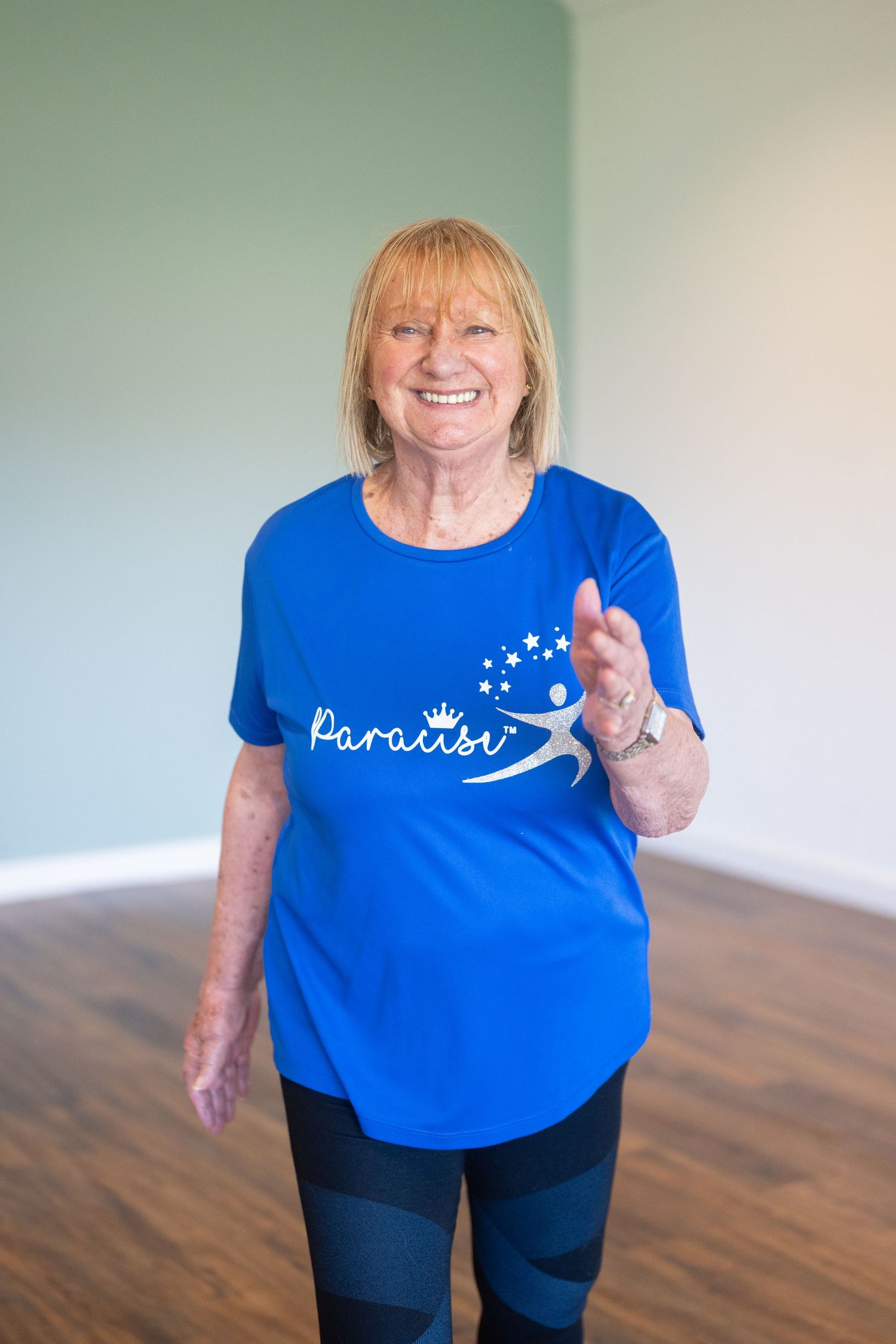 Fitness instructor wearing blue branded t-shirt demonstrating exercise moves in studio.
