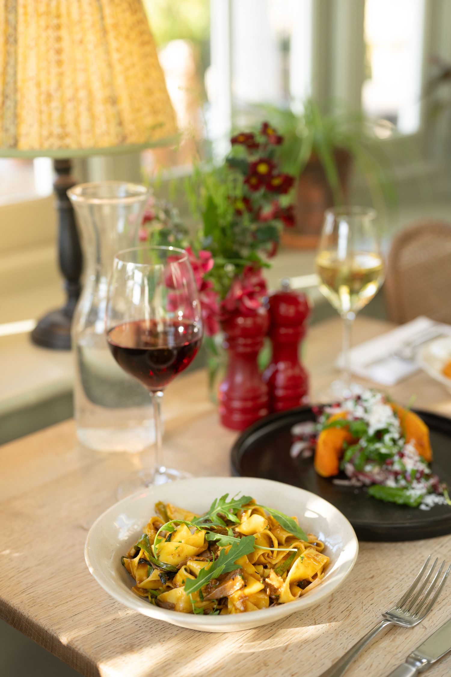 Elegant table setting with pasta dish, wine glasses and warm lighting in cozy dining room.