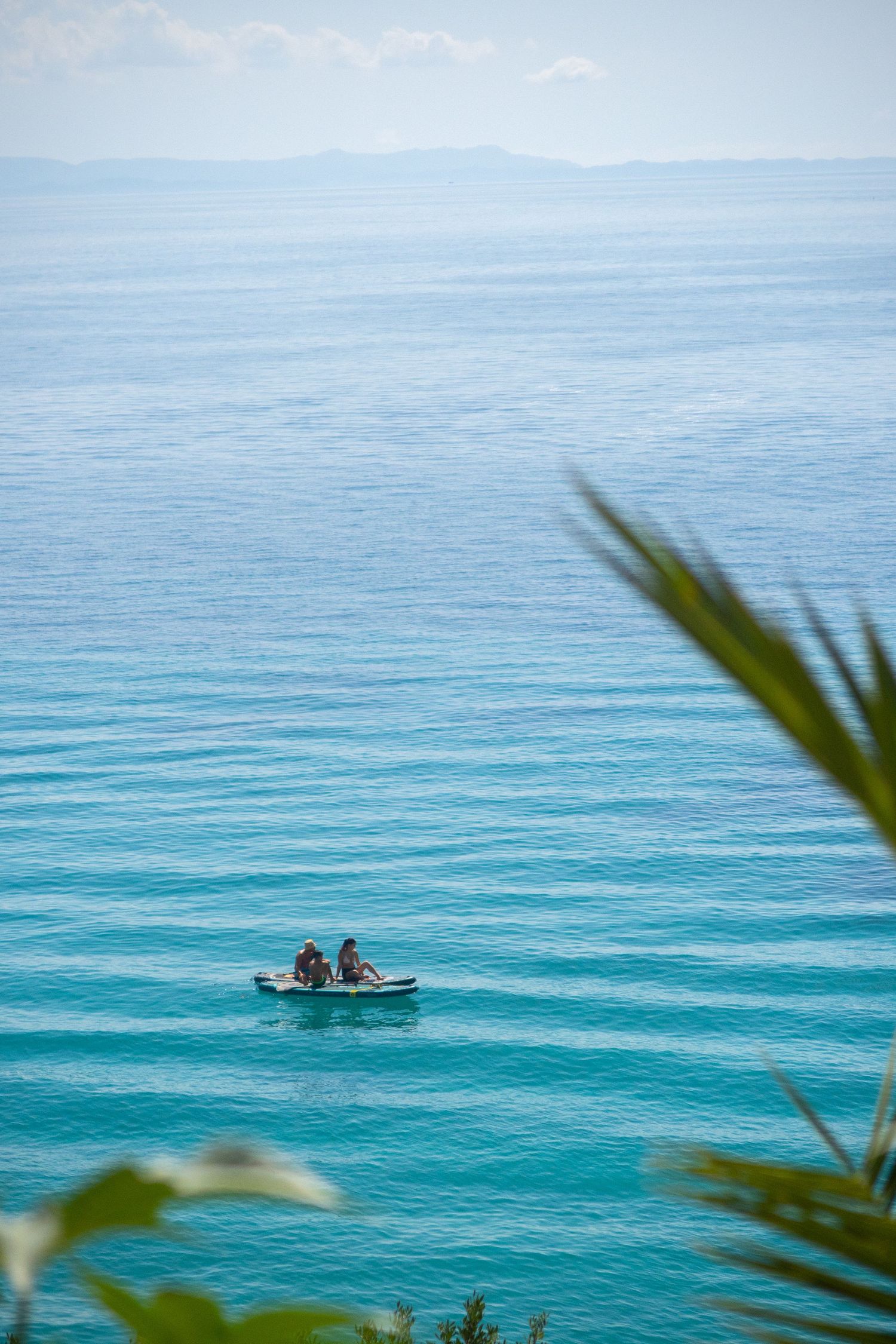 Small boat floating on pristine turquoise ocean waters viewed through palm fronds.
