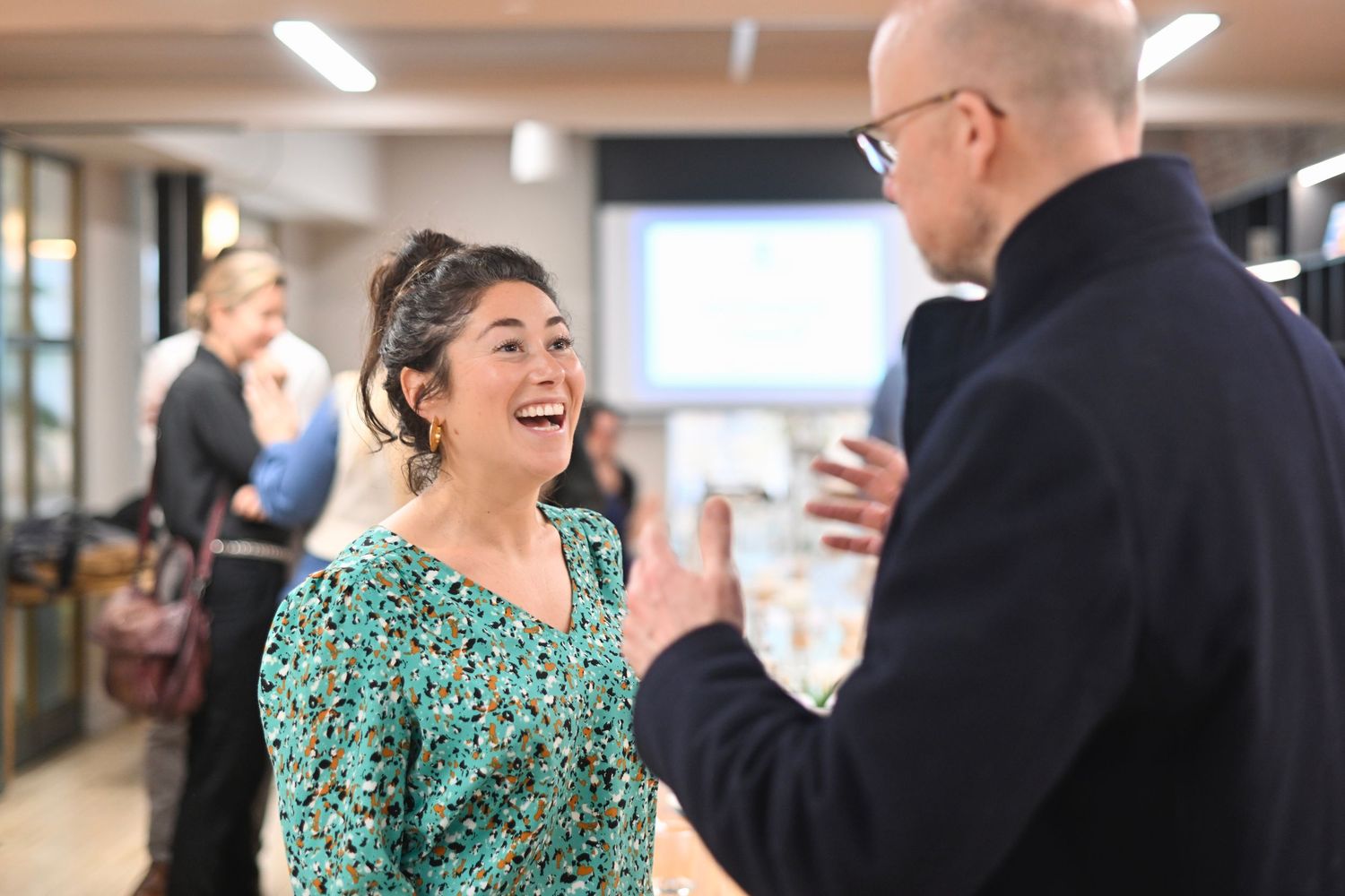 Professional networking event showing animated conversations between attendees in a bright indoor setting.