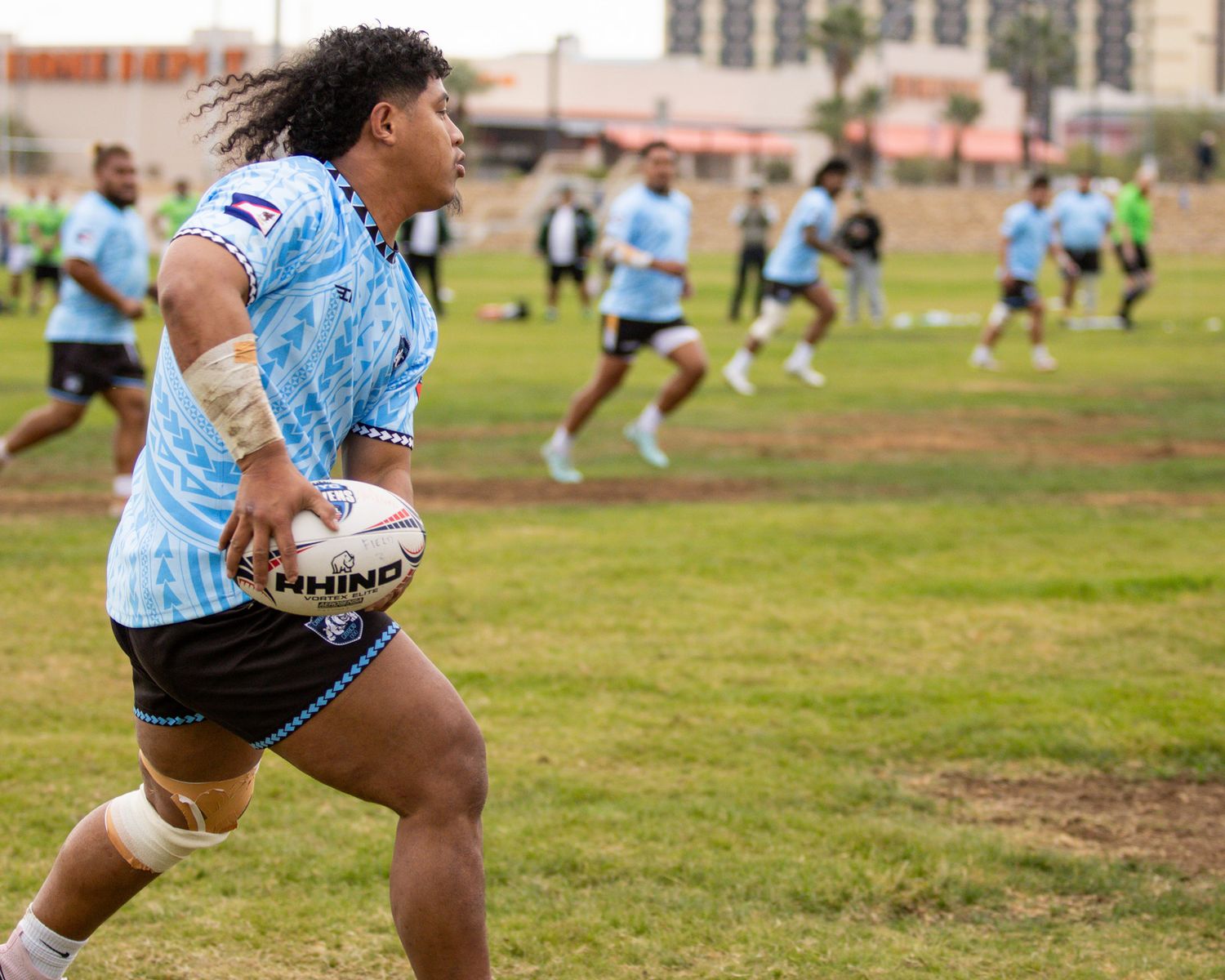 Rugby player in blue Sharks jersey carries ball during outdoor team training session on grass field.