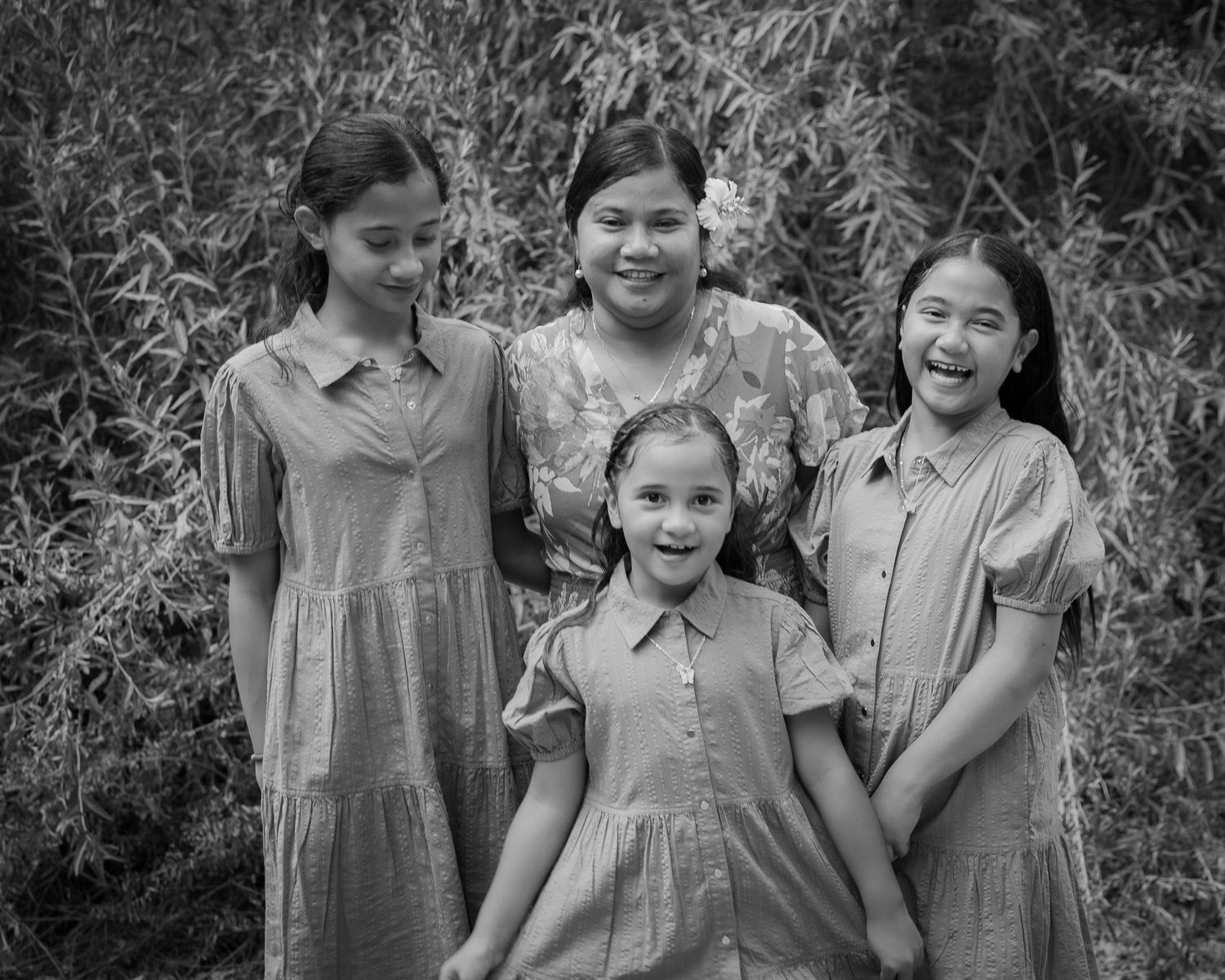 Black and white portrait of four young girls smiling together outdoors near lush green foliage.