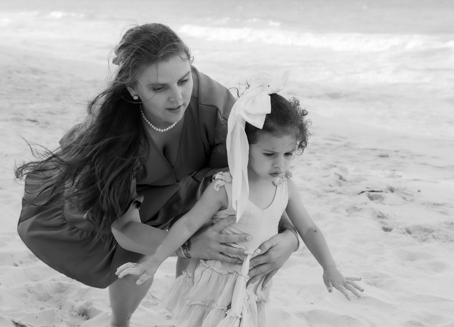 Woman and young girl playing on sandy Hawaiian beach in black and white photo, waves in background.