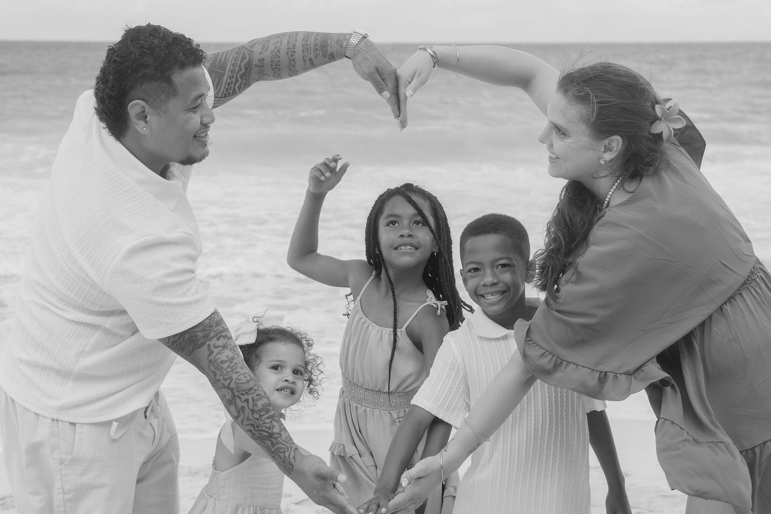 Black and white family photo of parents and three children playing together on a beach near the ocean waves.