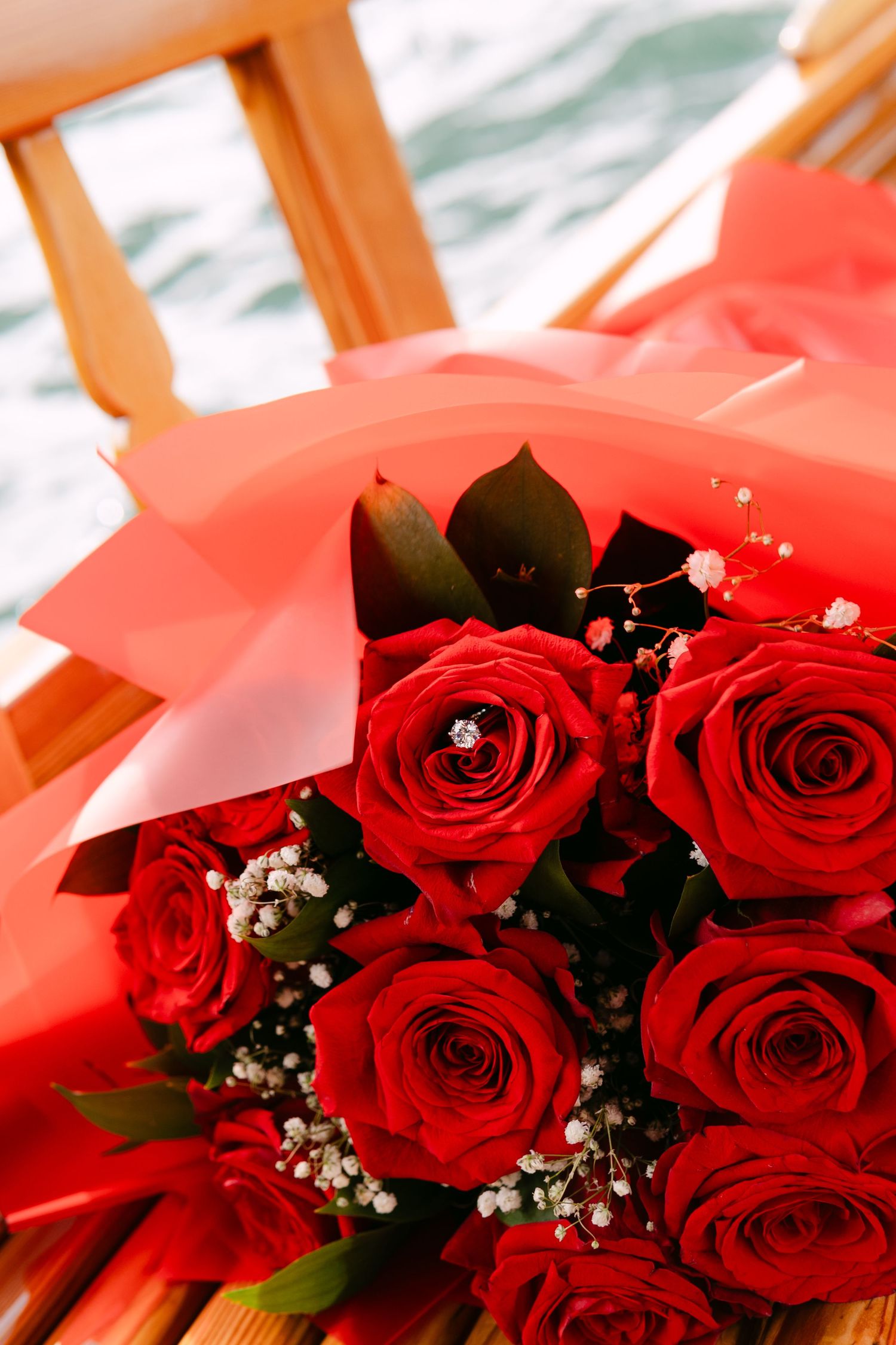 A close-up view of a luxury bouquet featuring deep red roses wrapped in festive paper during an outdoor pletna boat ride.