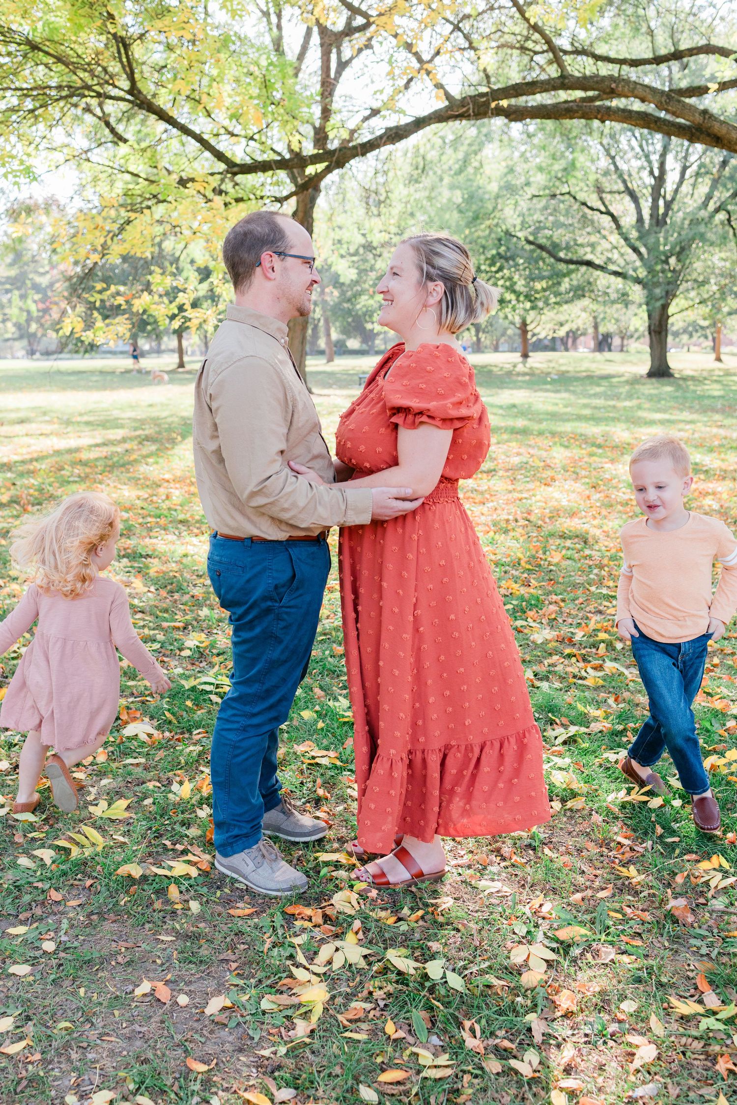 A family in coordinated fall outfits stands together among autumn leaves in a park setting.