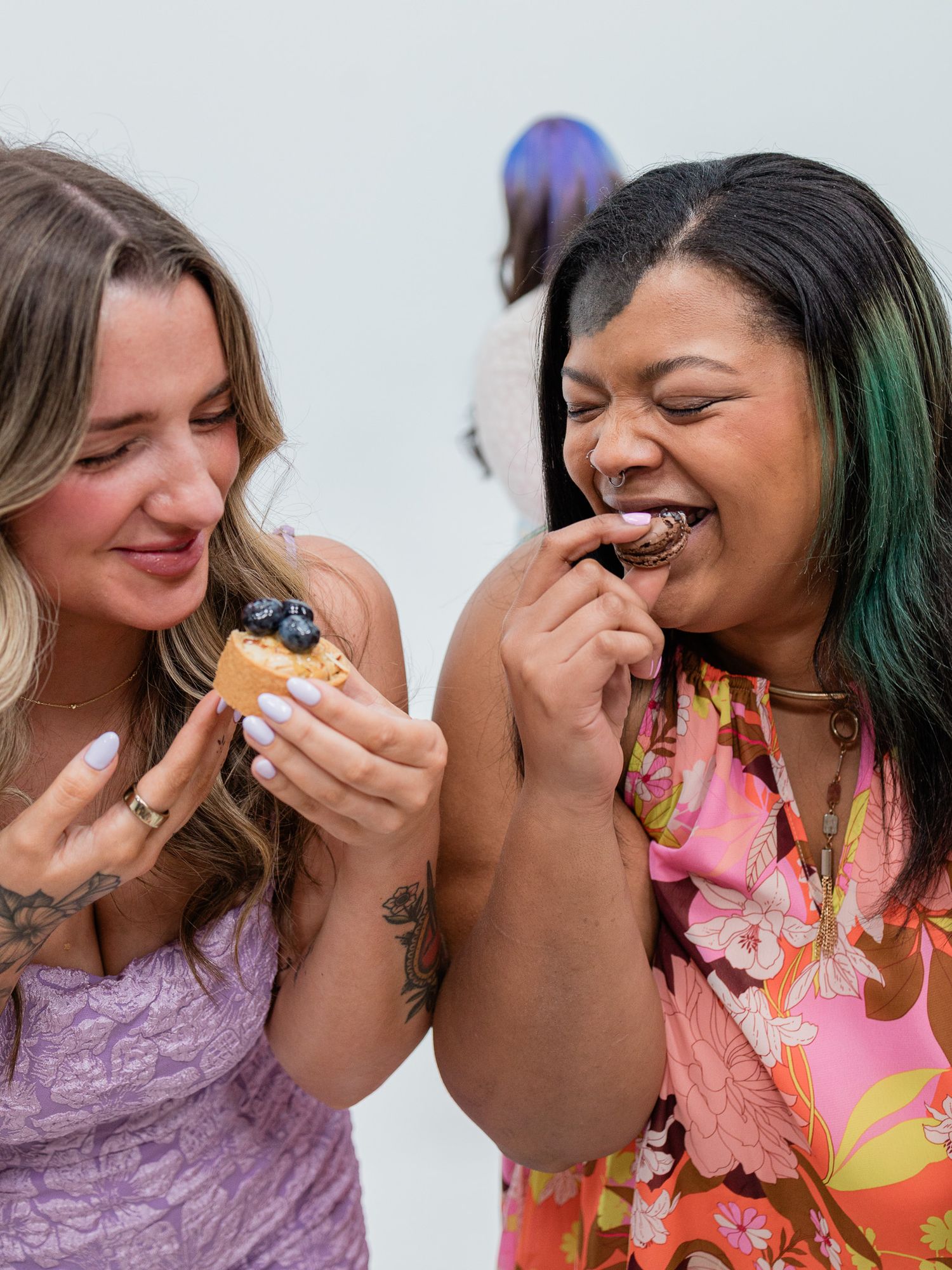 Two friends laughing while enjoying desserts together at an event.